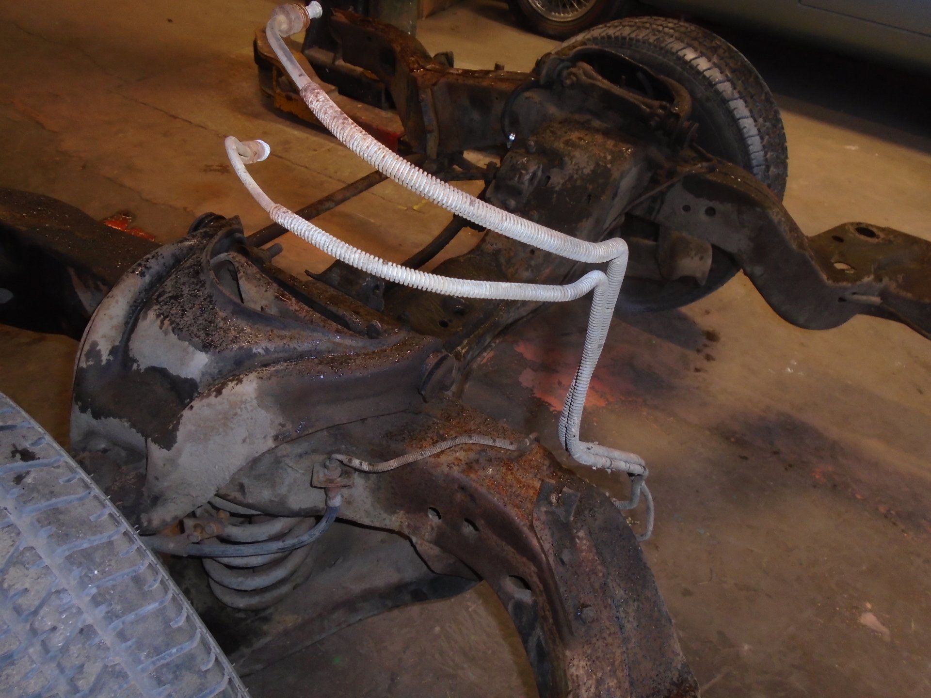 Rusty car chassis with a white fuel line, tire in the foreground.
