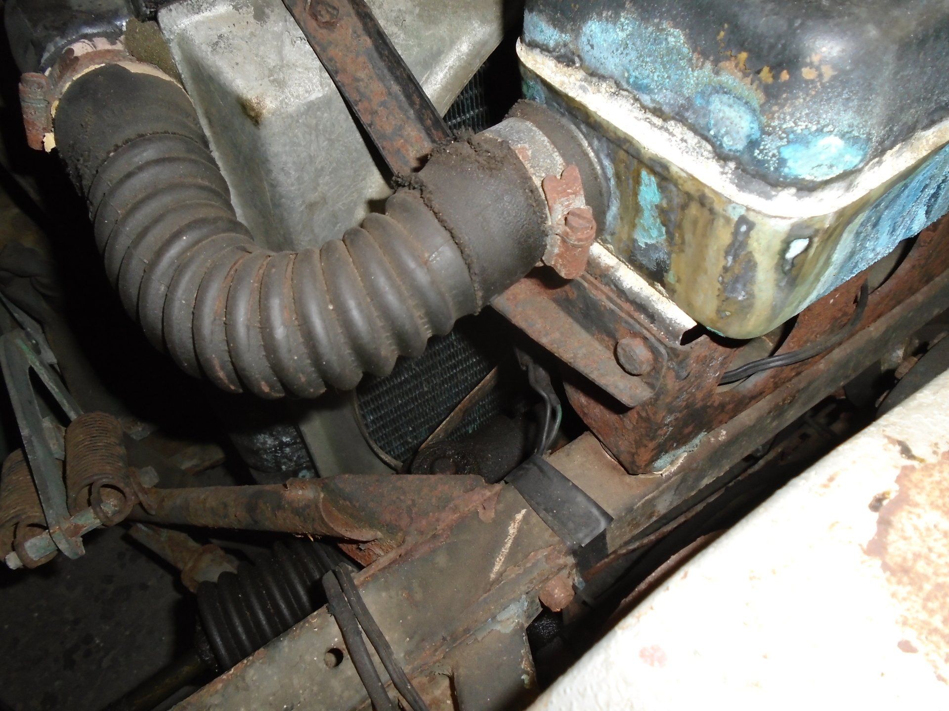Rusty car radiator with hose, brackets, and a blue-painted top.
