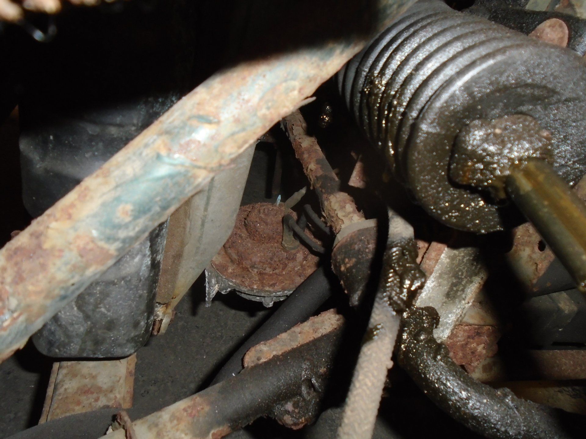 Rusty car steering components with leaking fluid.