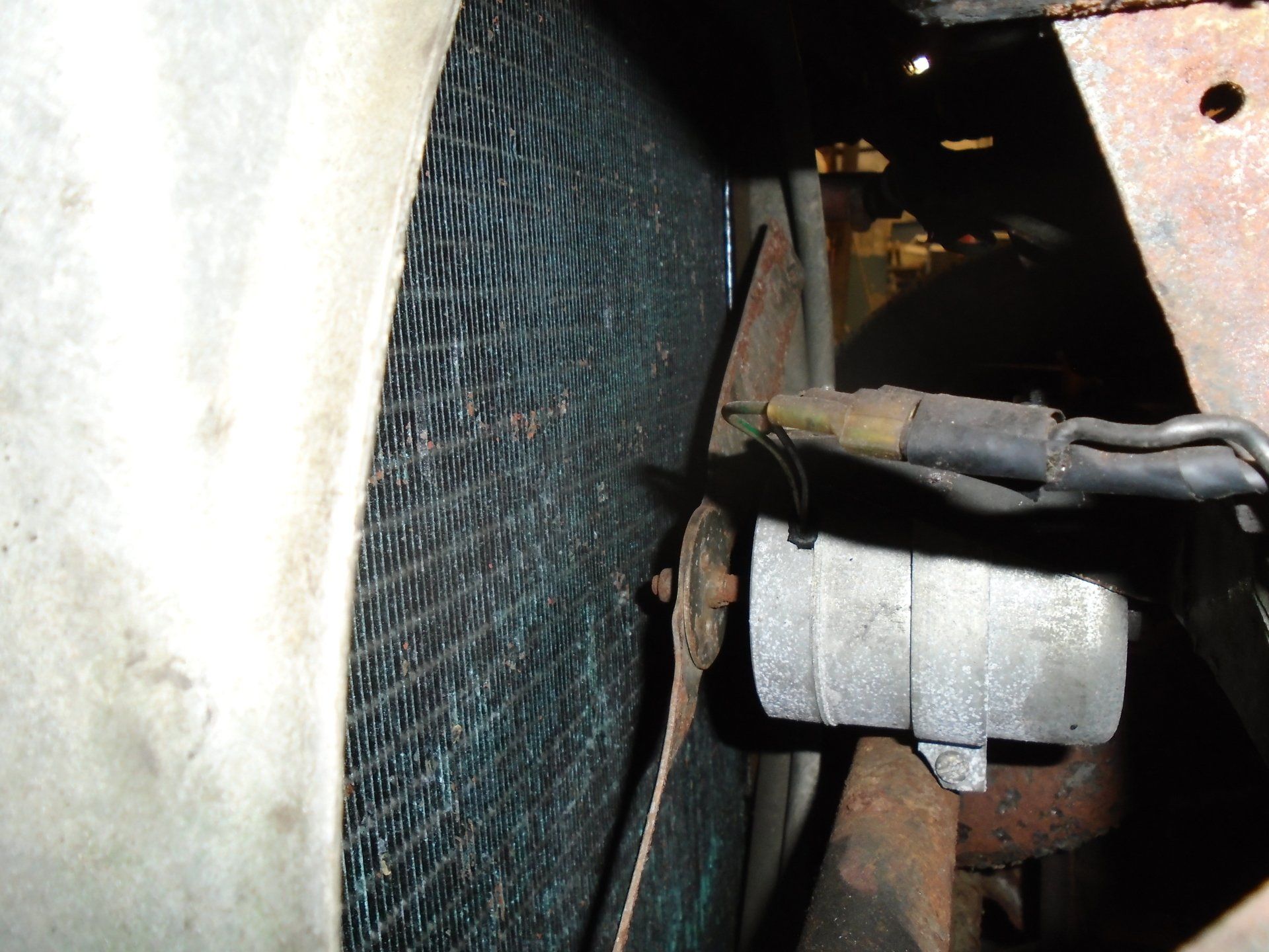 Close-up of a radiator fan assembly with a metal fan blade, next to a mesh radiator and part of an engine.