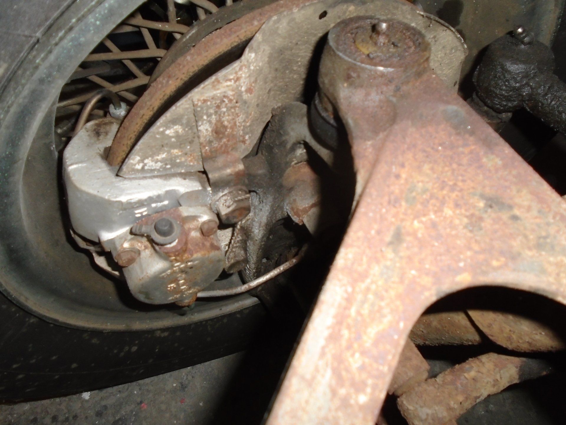 Rusty car brake assembly. Wheel, caliper, and suspension components visible.