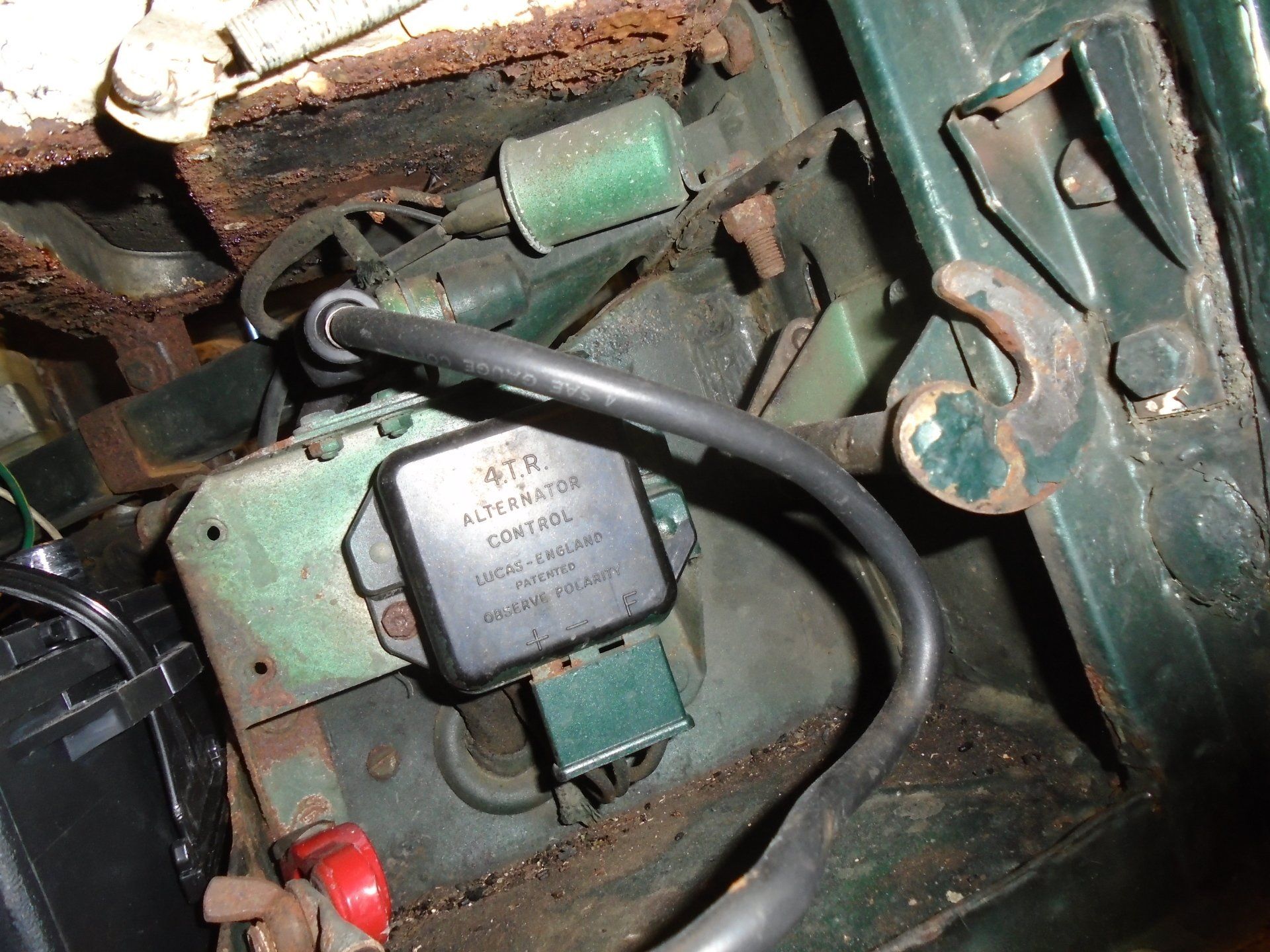 Engine compartment with a green regulator, rusty metal, and black wiring.