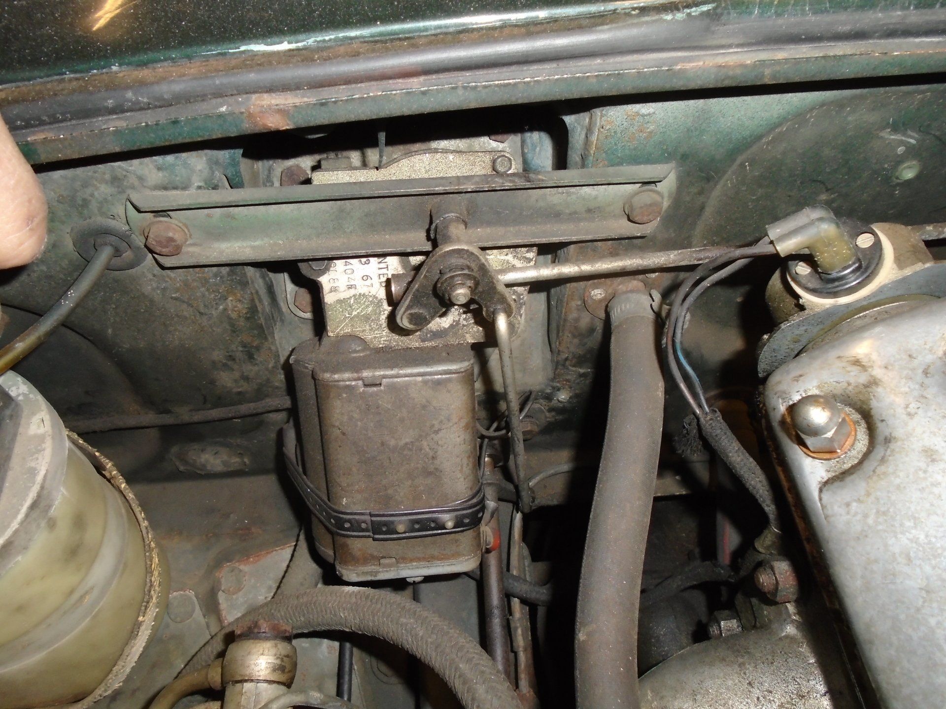Close-up of car engine parts. A rectangular black box and metal bars are mounted against a green surface.