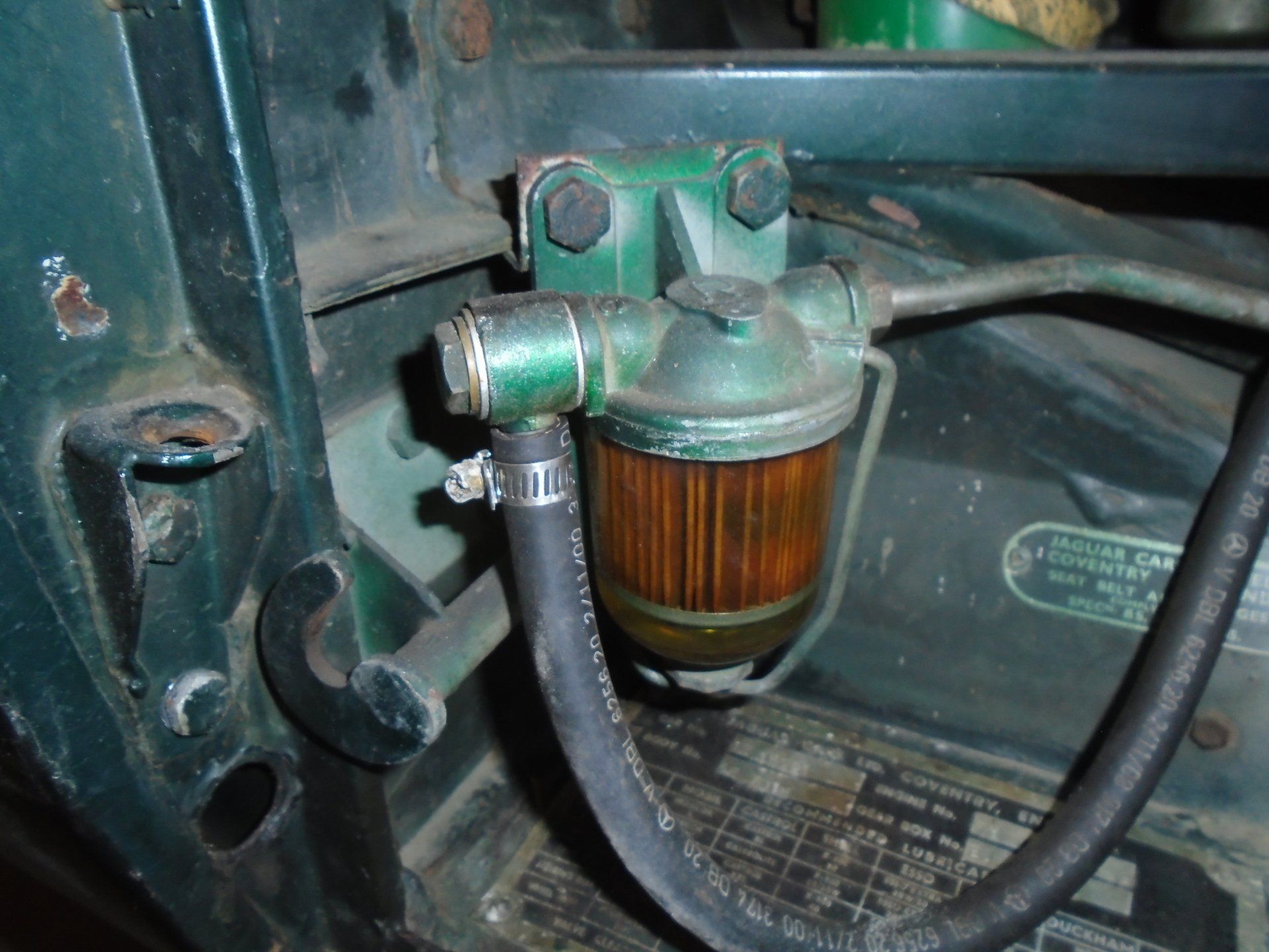 Green fuel filter on a vintage vehicle, connected by hoses, mounted to the car's body.