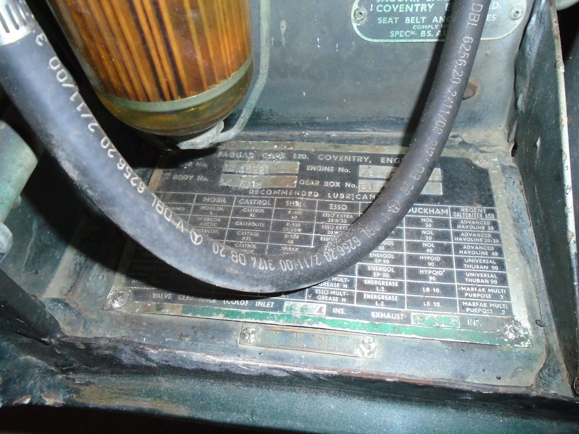 Close-up of a vehicle's metal plate with text and numbers, covered partially by a black hose and a filter.