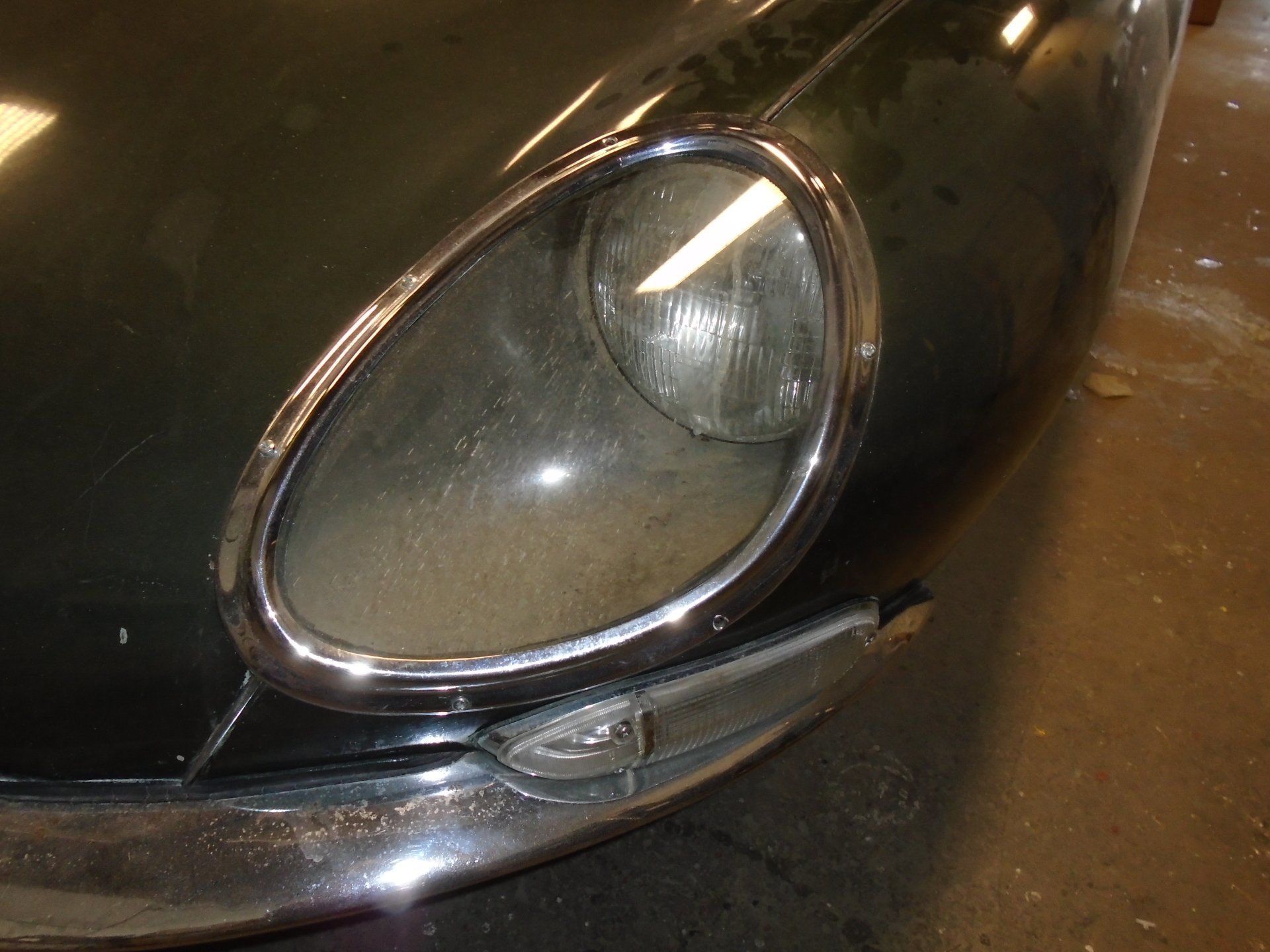 Close-up of a vintage dark green car's headlight, dusty and chrome-rimmed.