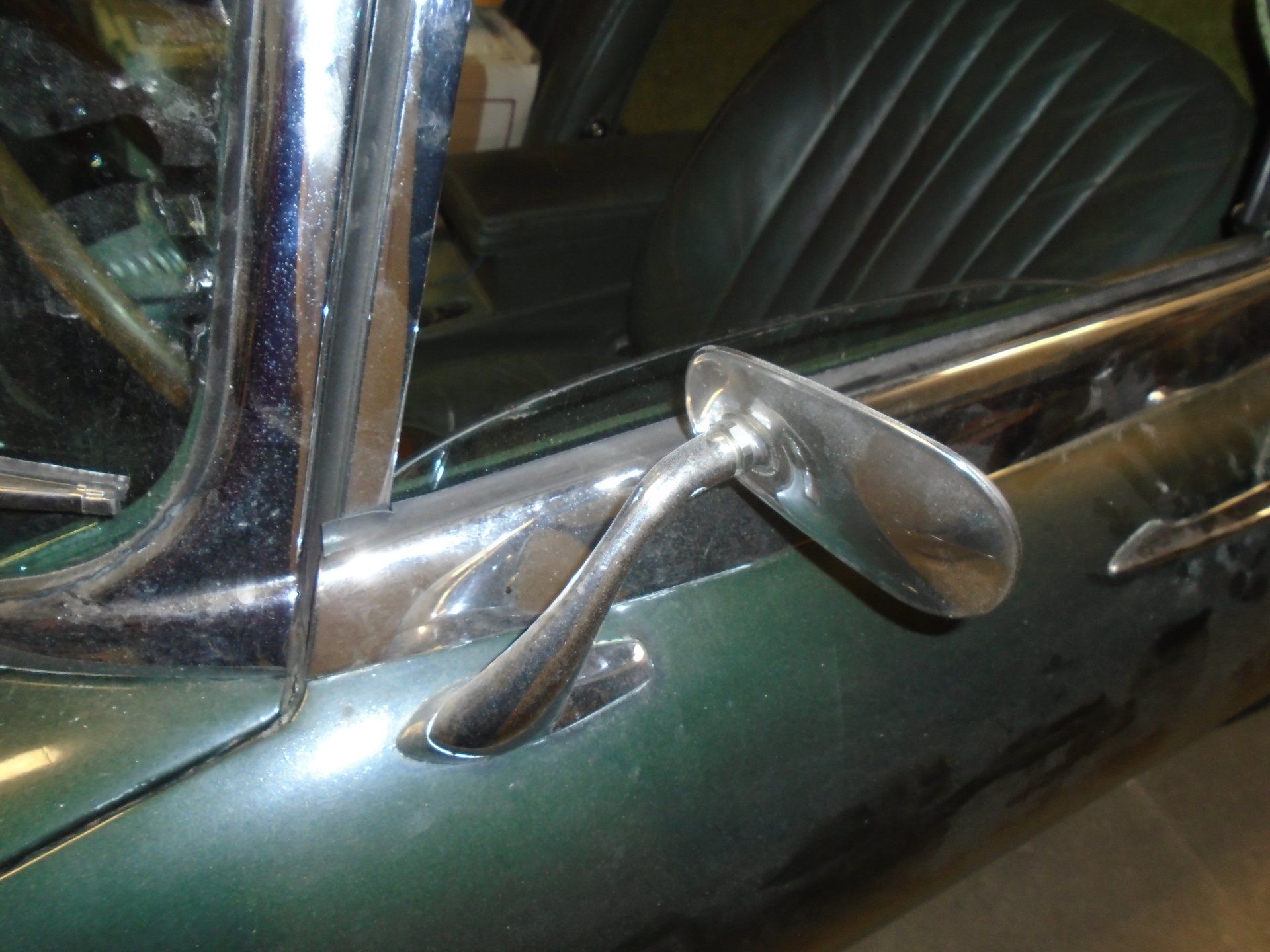 Chrome side mirror on a classic green car. Interior with green leather seat visible.