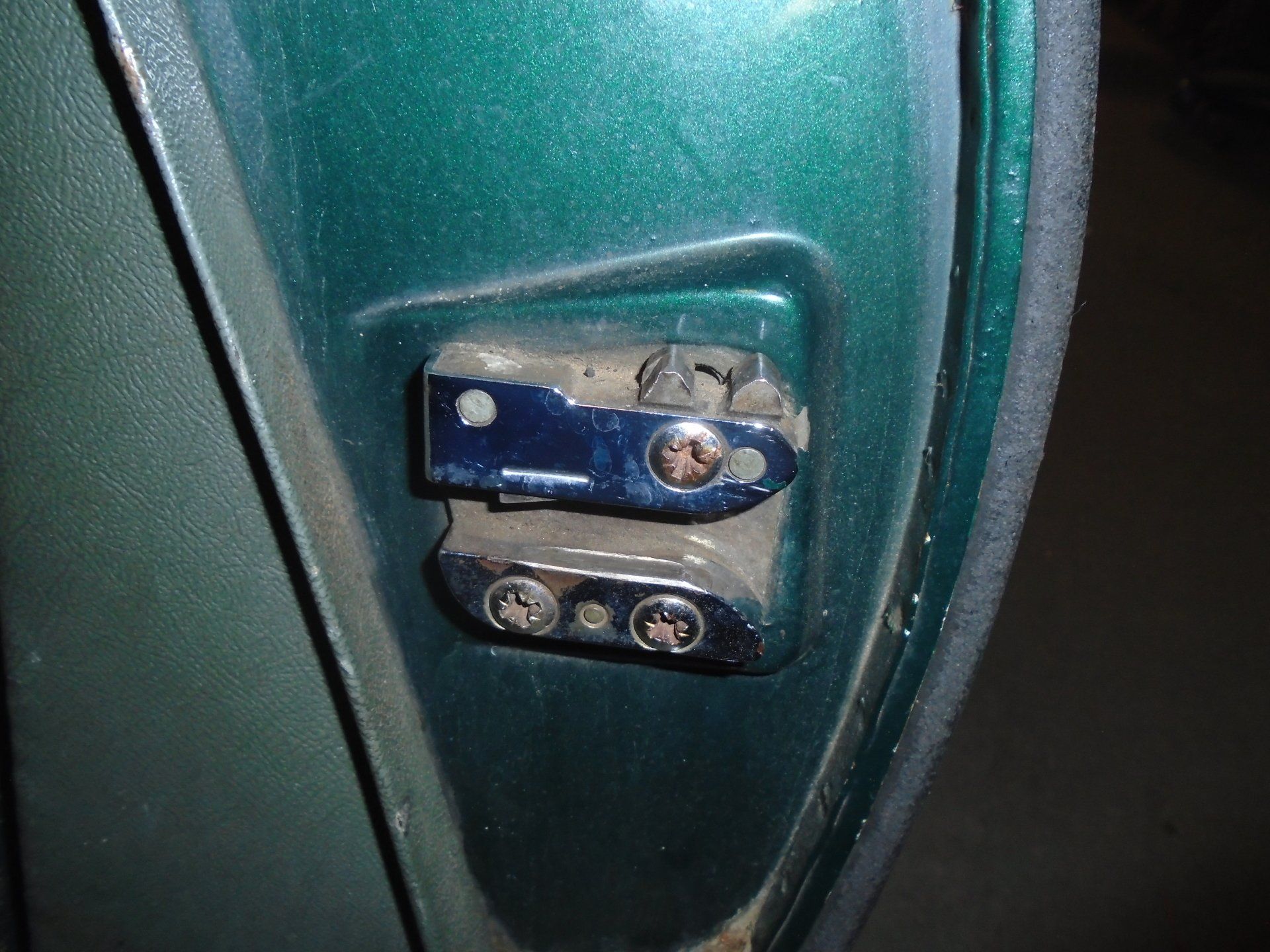 Close-up of a teal car door latch with two metal pieces and screws, near door frame.