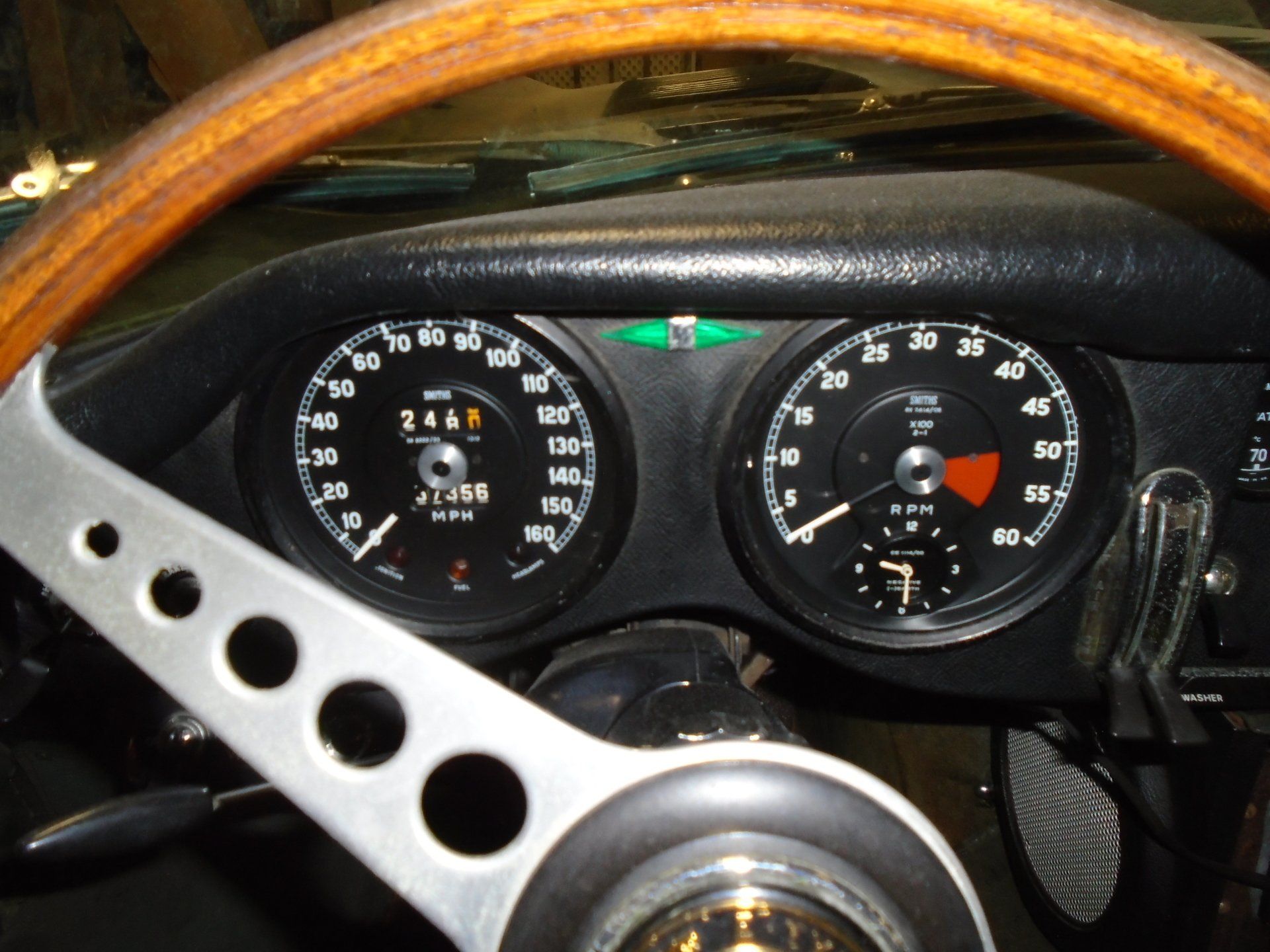 Dashboard of a classic car, showing speedometer and tachometer gauges, with a wooden steering wheel in view.