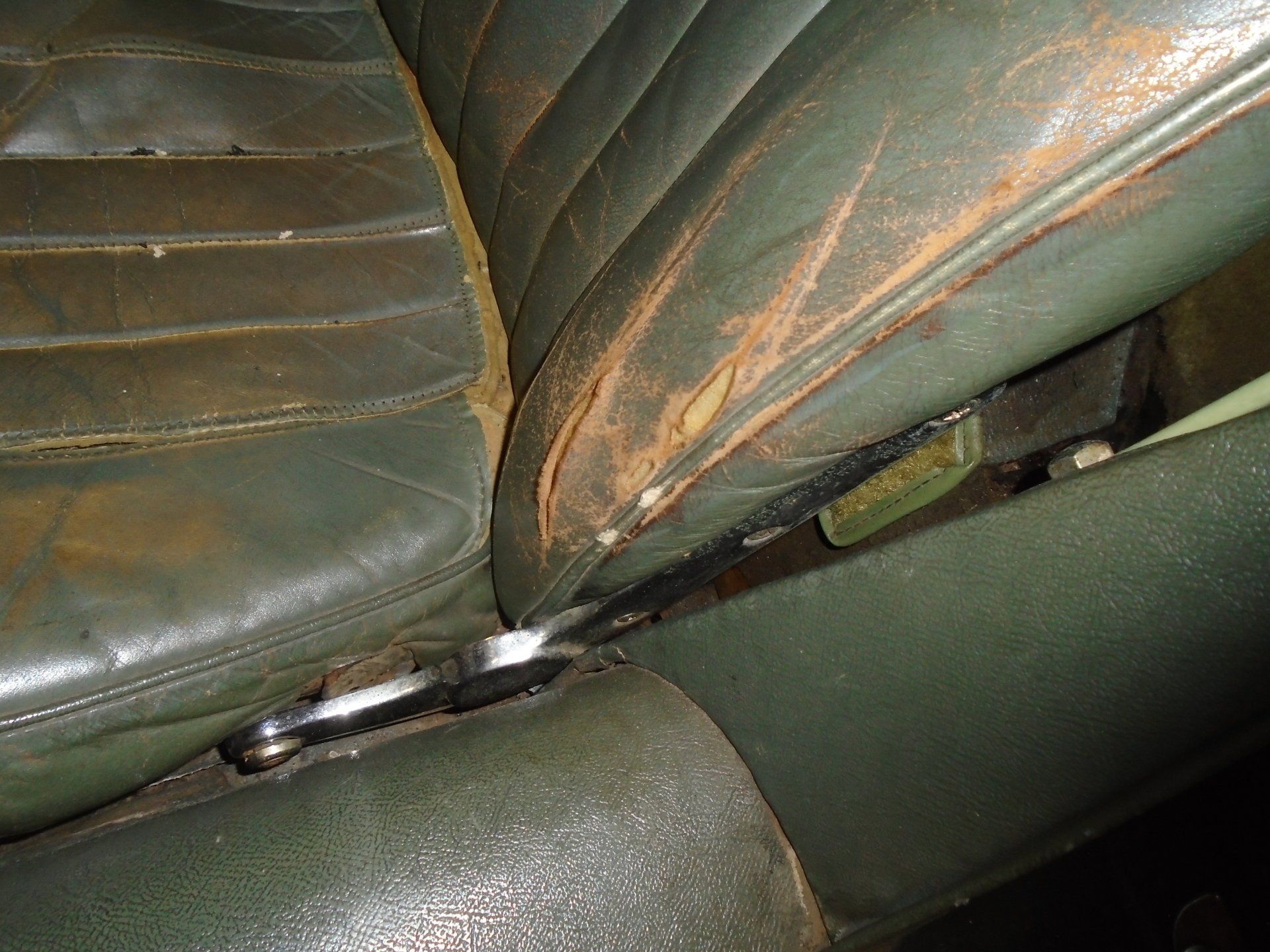 Green leather car seat with wear and tear, close up showing the base and adjustment mechanism.