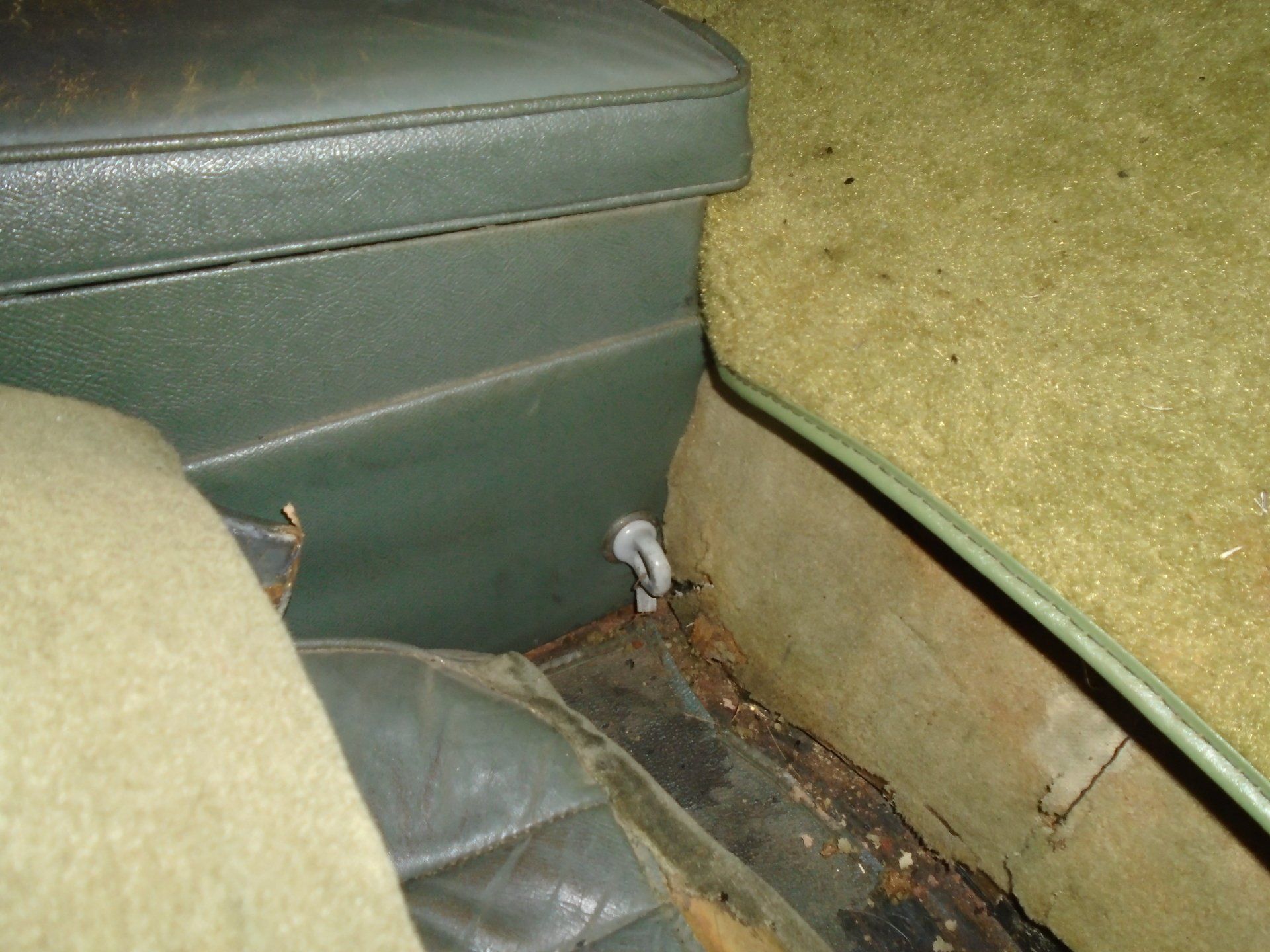 Green car interior with seat, panel, and carpet. Corrosion visible on floor.