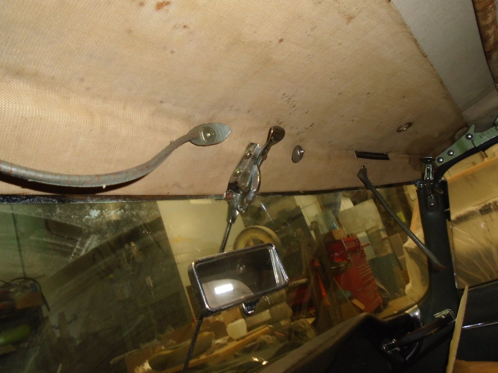 Interior car view: stained headliner, rearview mirror, chrome lever, grab handle, and windshield.