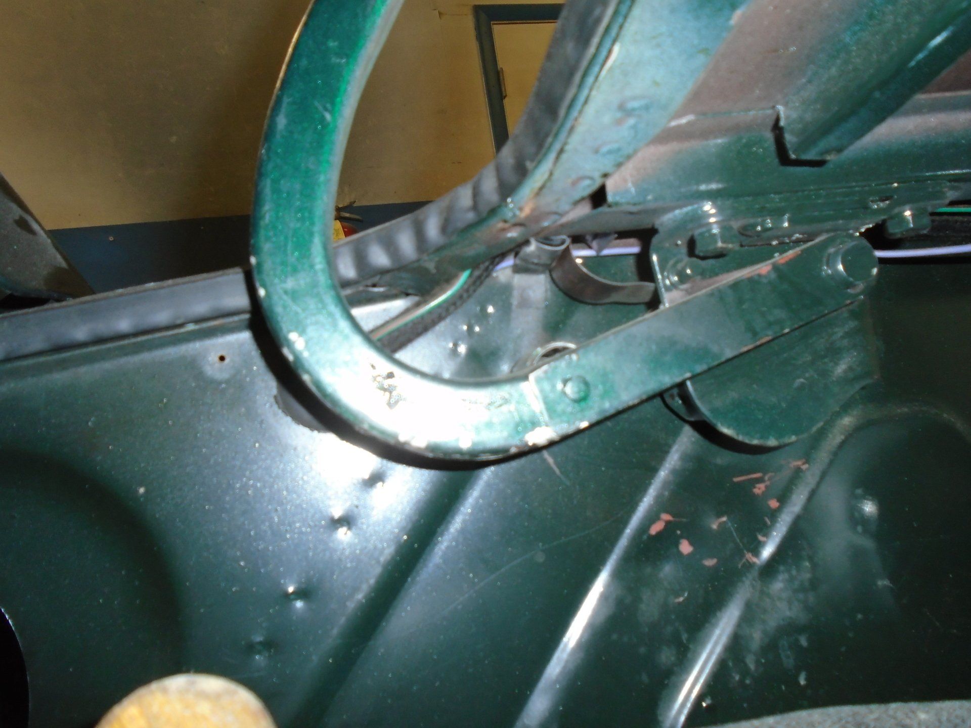 Green metal frame and hinge attached to a vehicle's body.