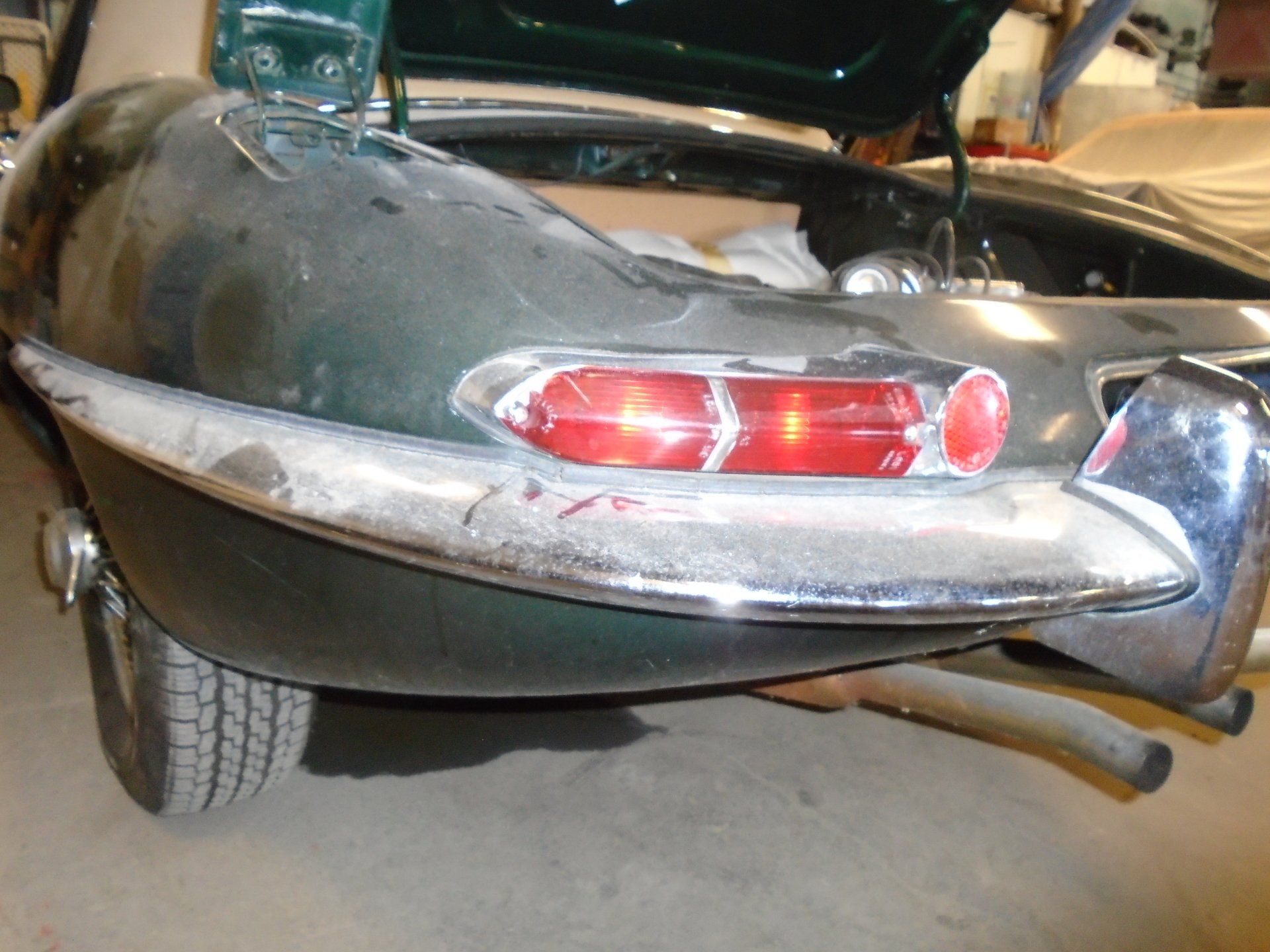 Rear view of a dark green vintage Jaguar E-Type car with chrome trim and a red taillight.