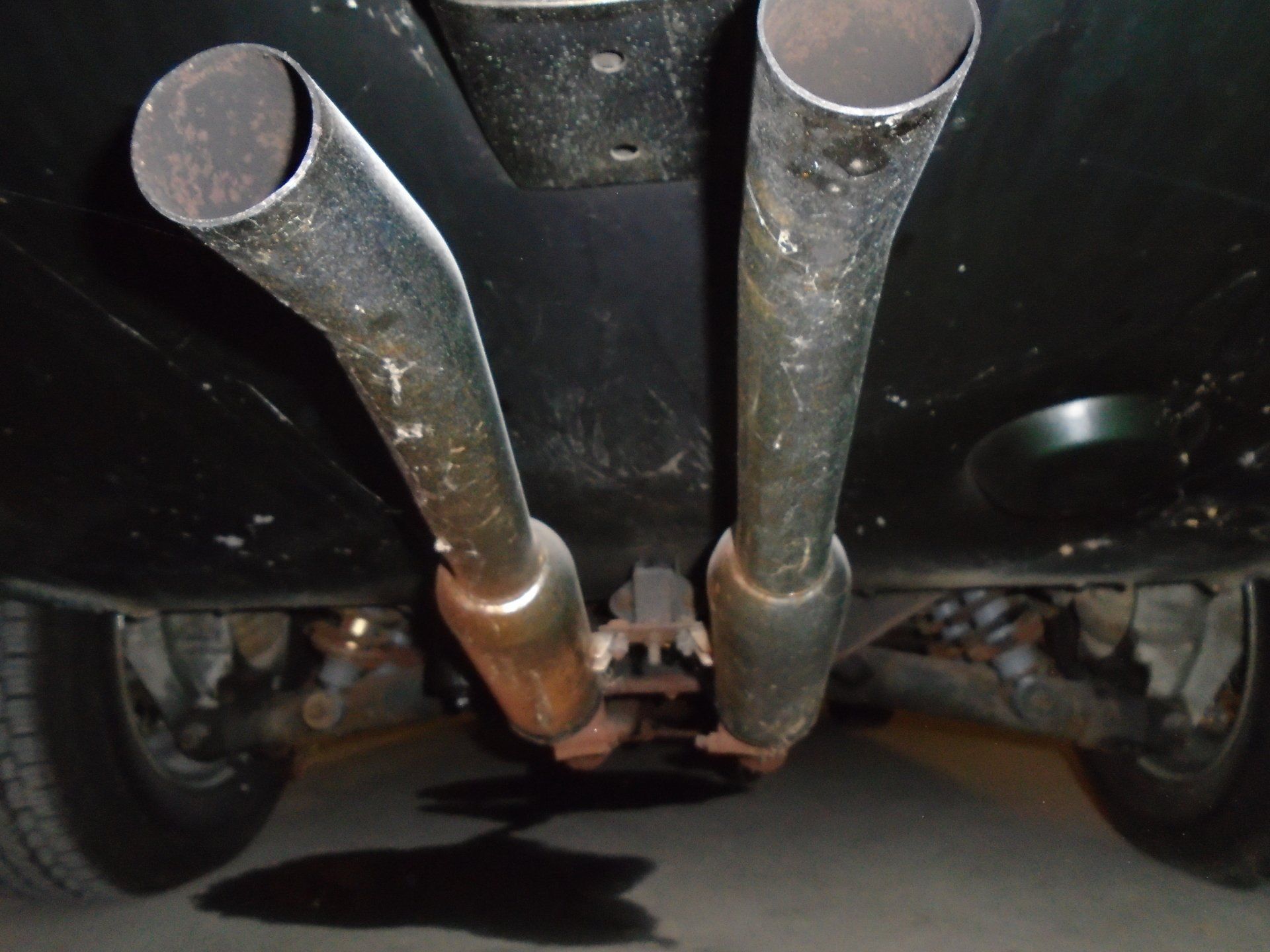 Underside of a vehicle showing dual exhaust pipes, a black chassis, and a dark puddle below.