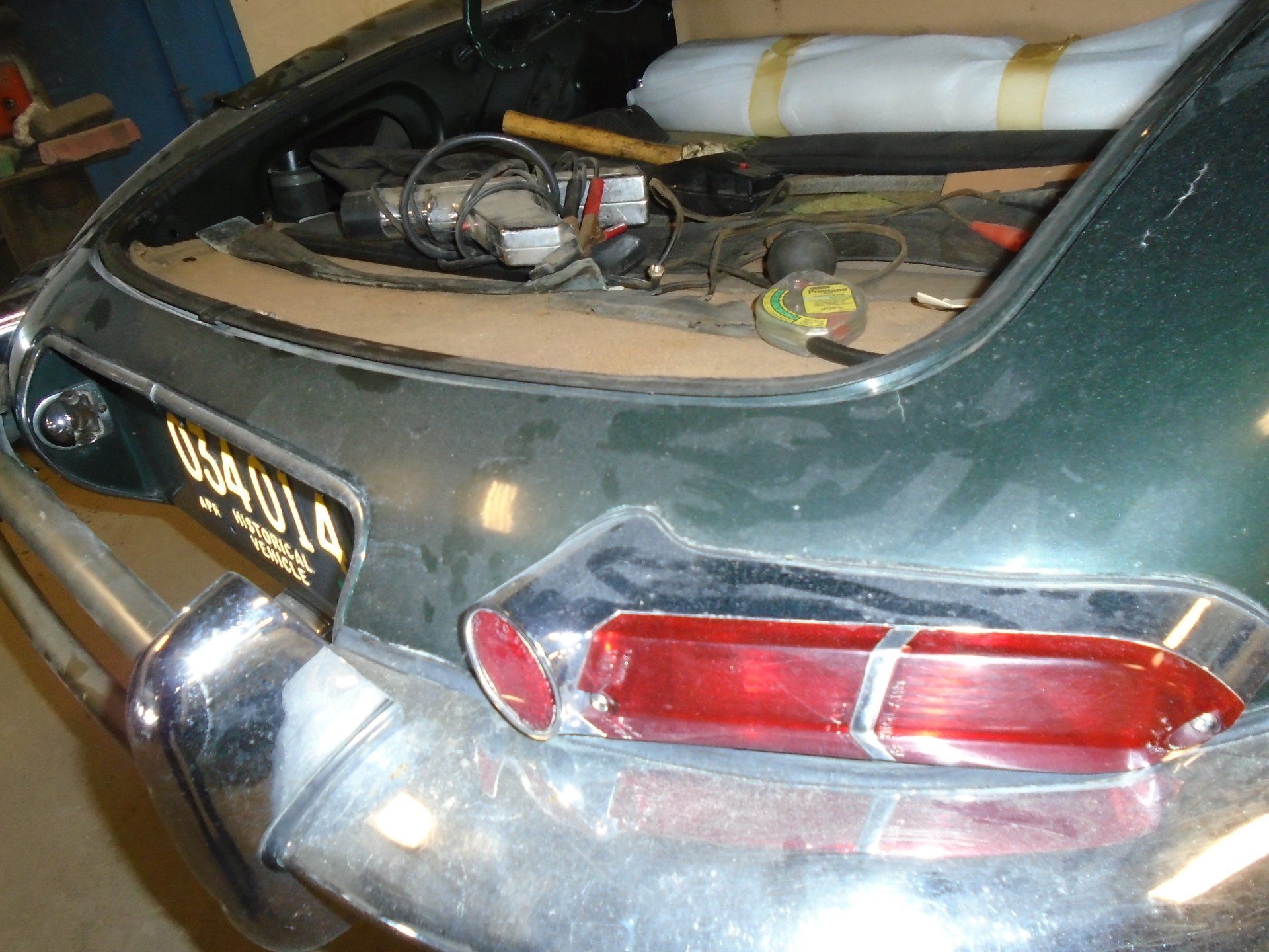 Green Jaguar car trunk open, various tools inside, license plate visible, chrome bumper.