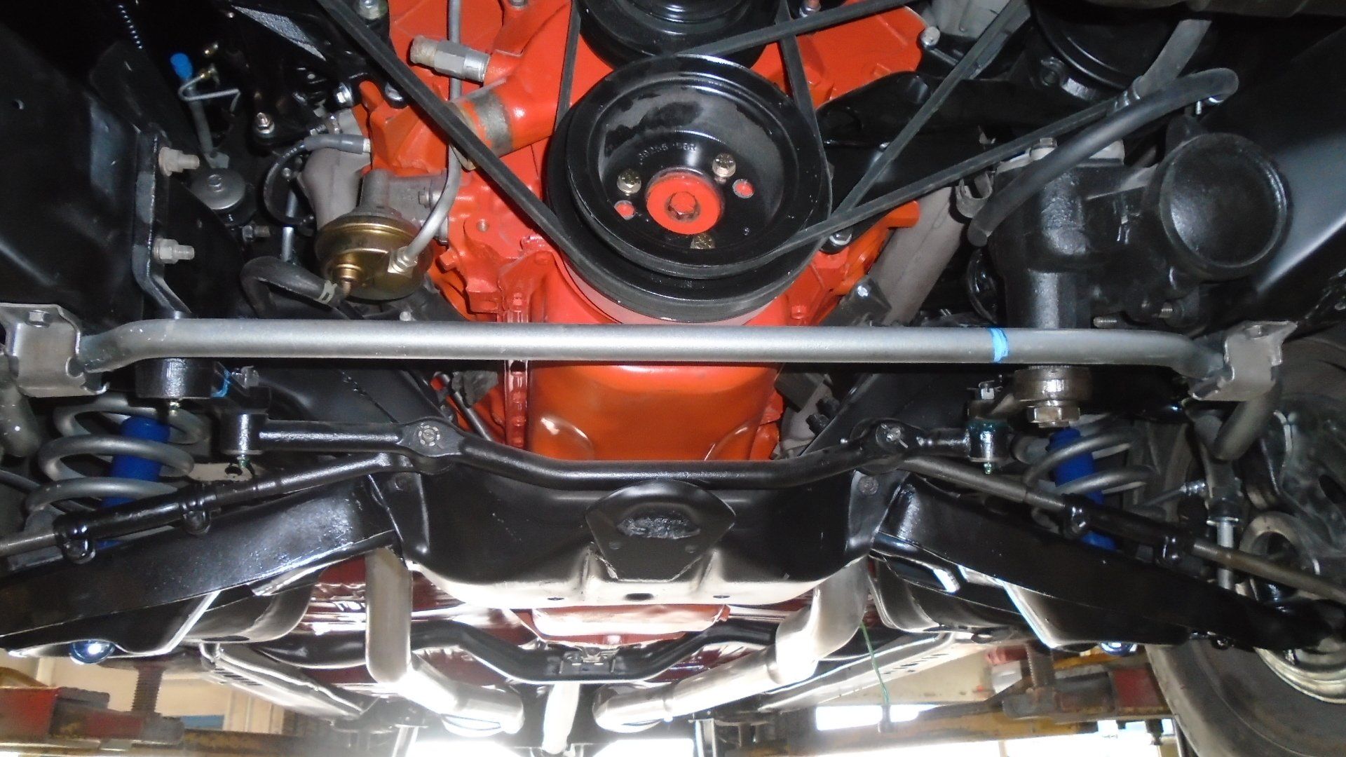Underside view of a classic car's engine, painted orange, with a black frame and components.