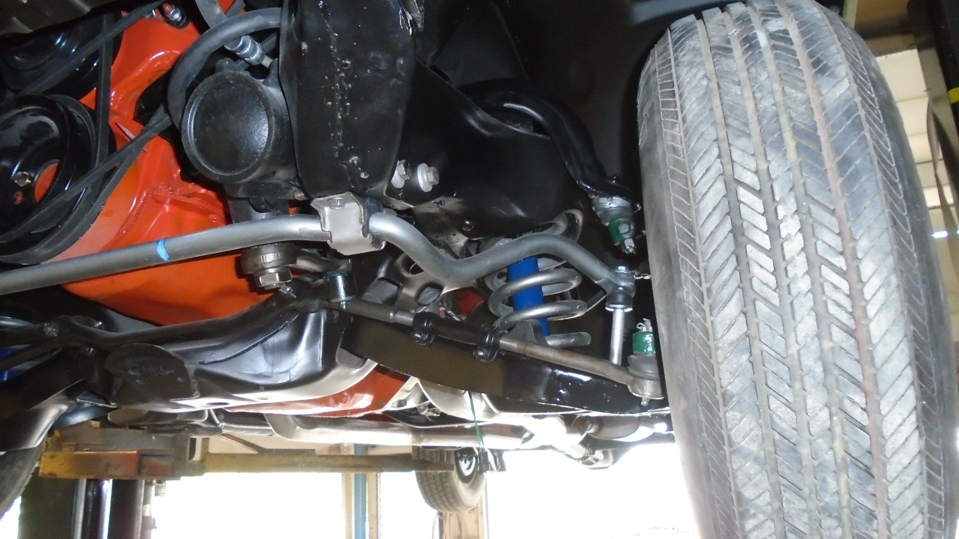 Undercarriage of a classic car, showing suspension, anti-sway bar, and orange engine block. Tire on the right.