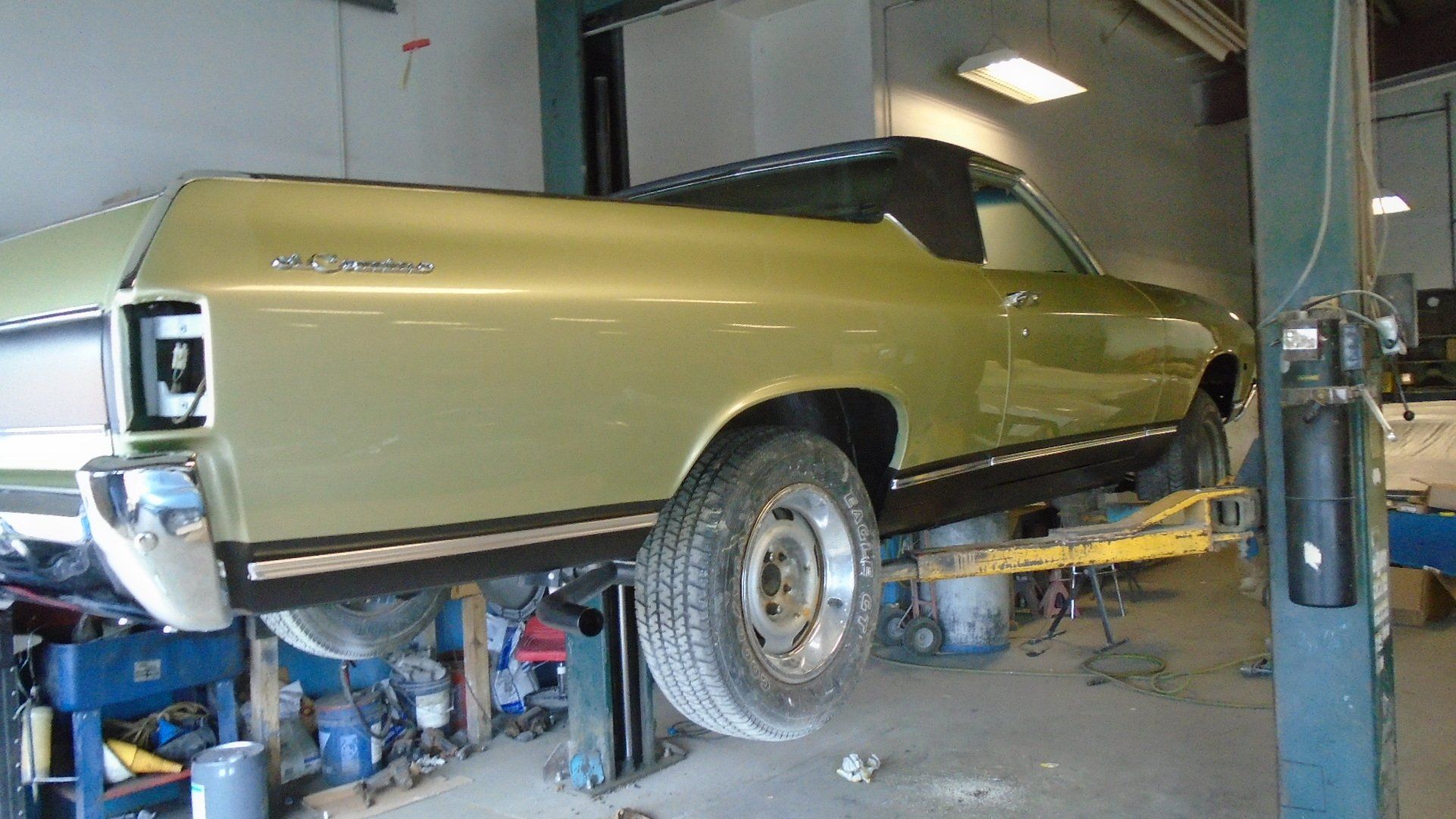 Green El Camino on a car lift in a garage.