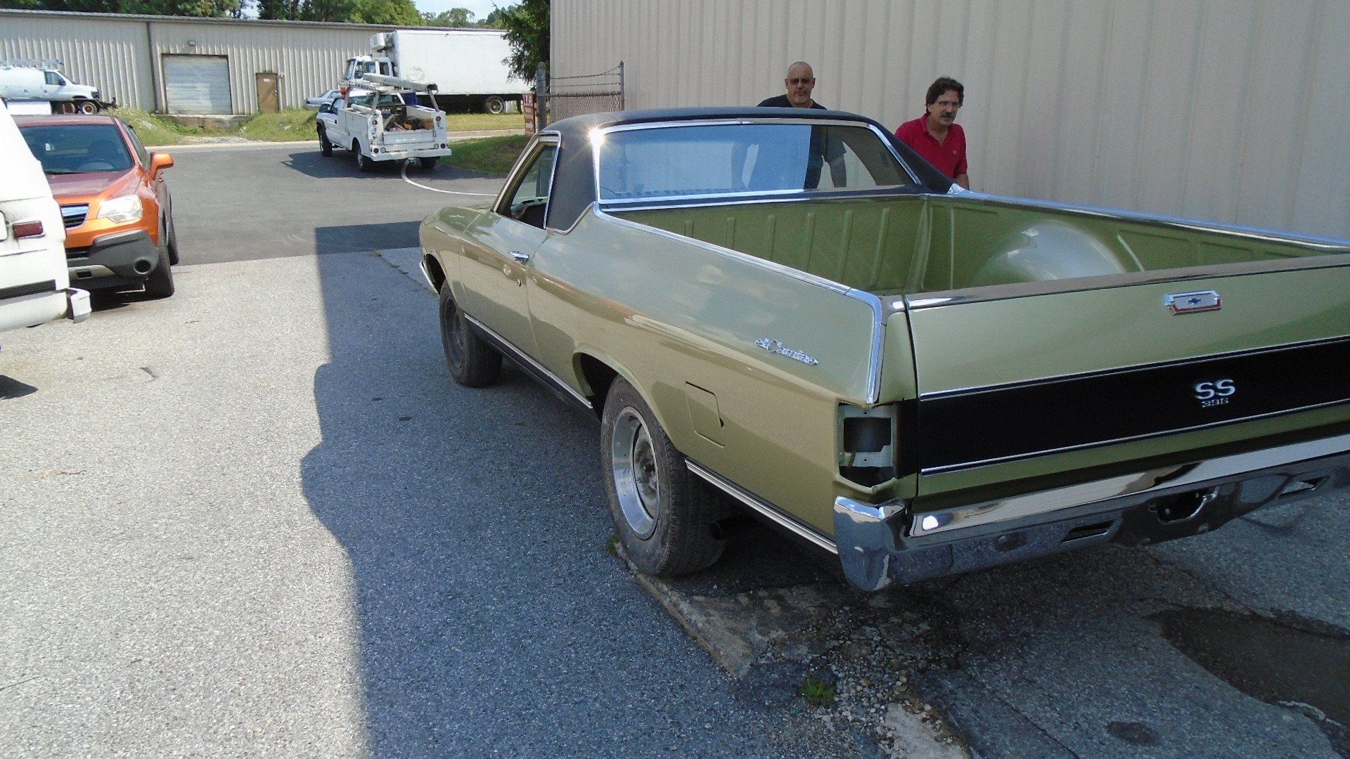 Green El Camino pickup truck parked on asphalt, two people near it, sunny day.