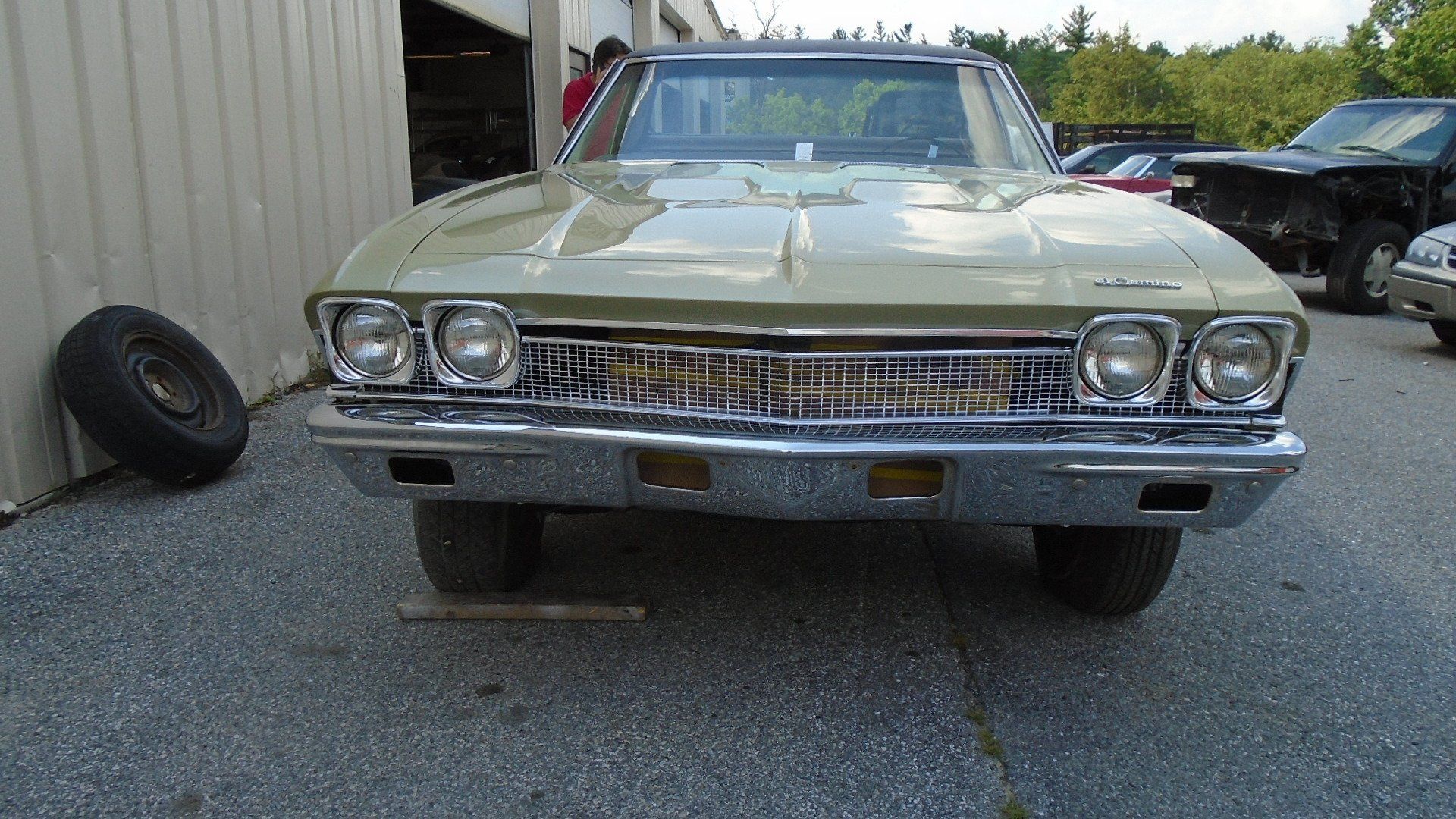Green classic car with chrome details parked outside a garage. Spare tire visible.