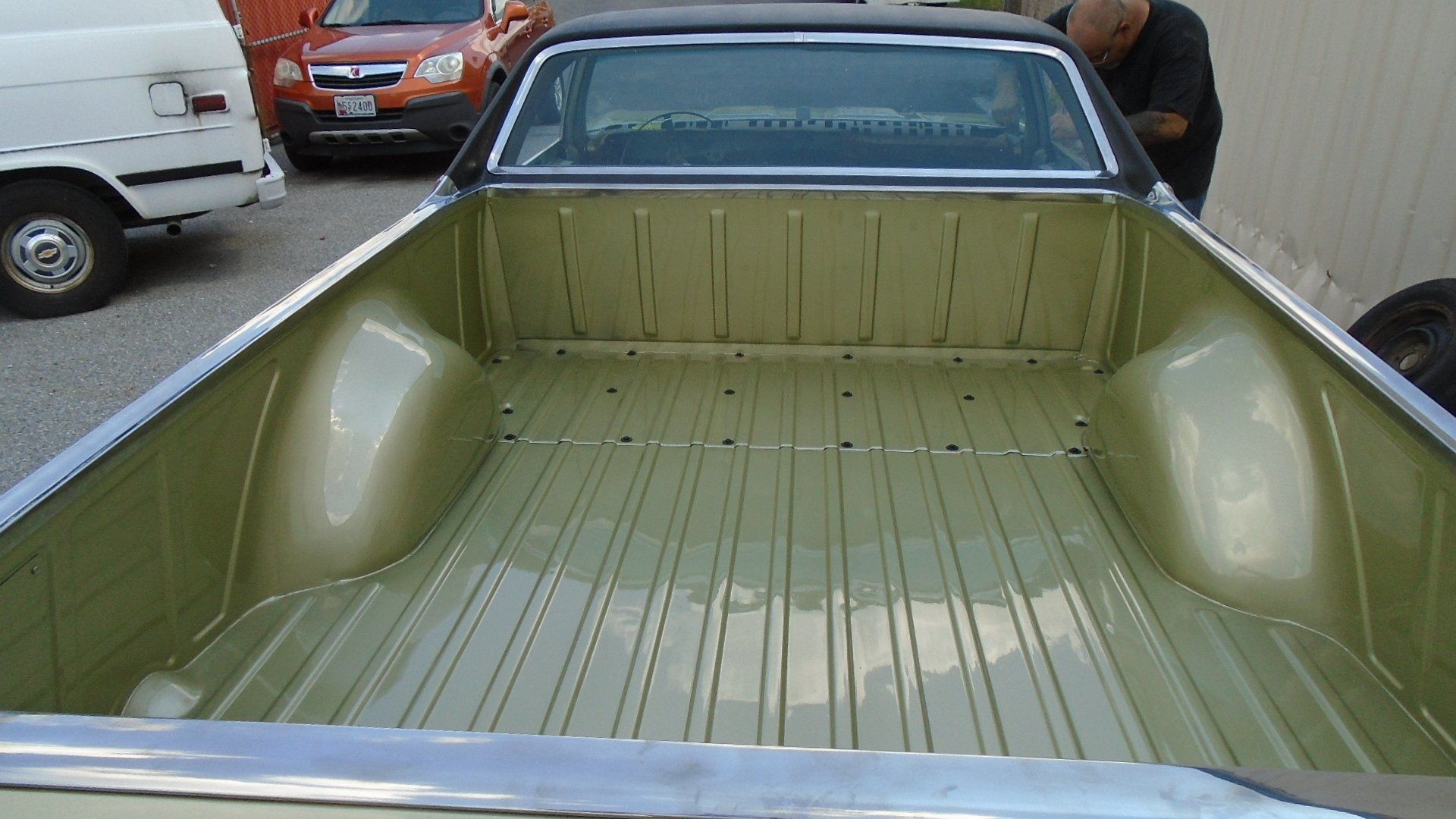 Gold-colored pickup truck bed with chrome trim; a person looks at it; other vehicles are in the background.