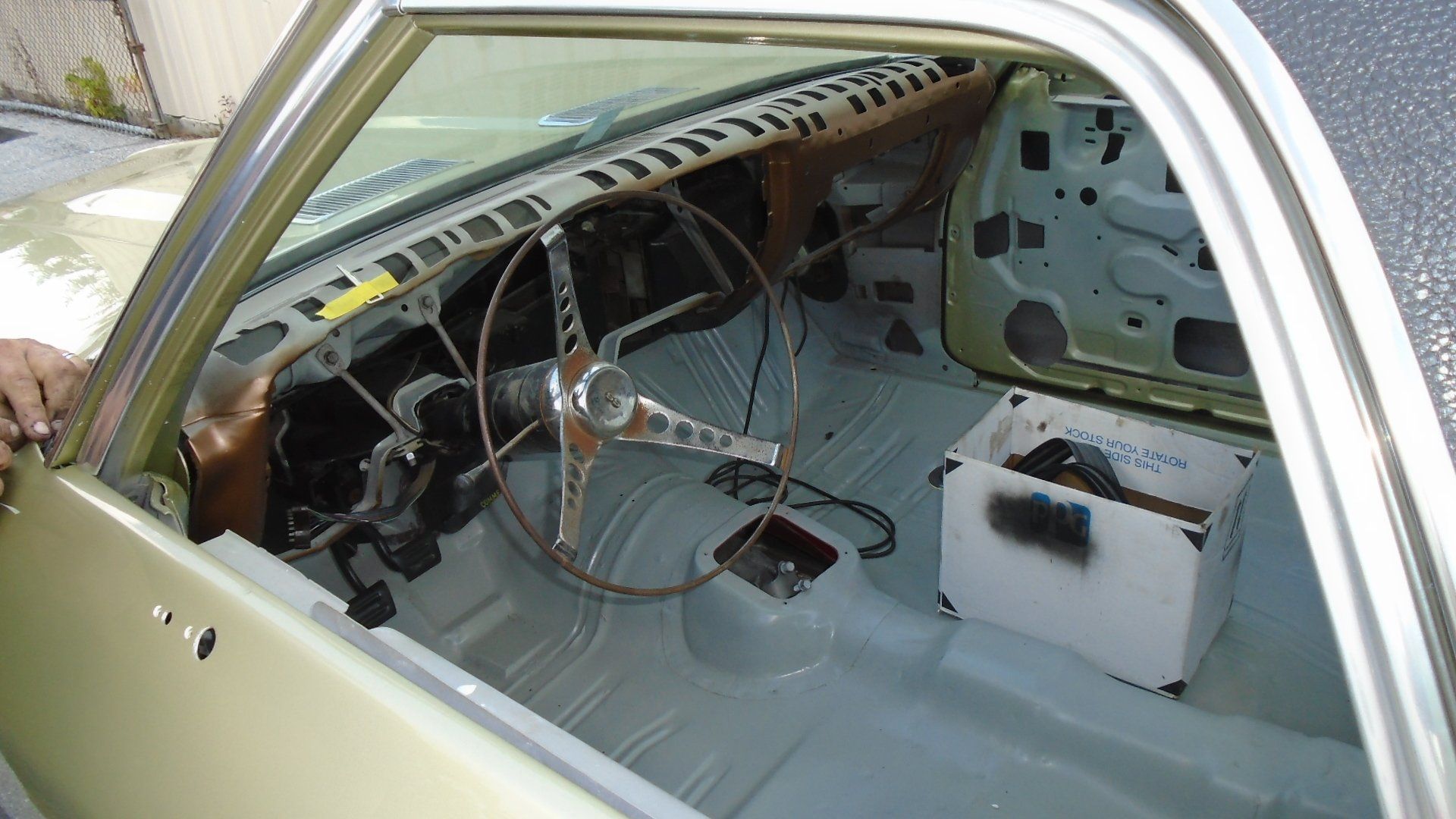 Interior of a classic car stripped down for restoration. Steering wheel, dashboard and floor visible.