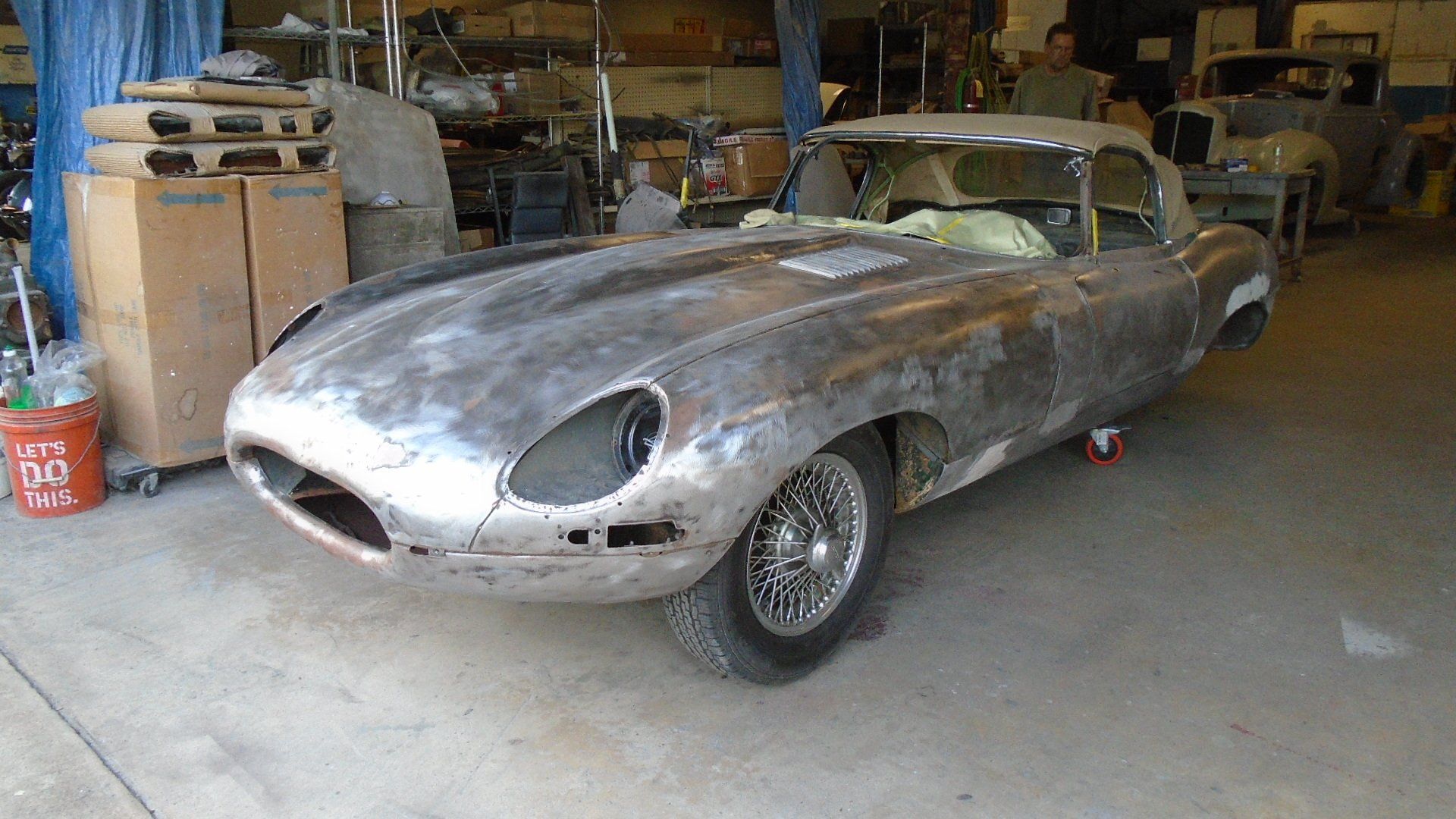 Jaguar E-Type convertible in a repair shop, body stripped down, wheels on.