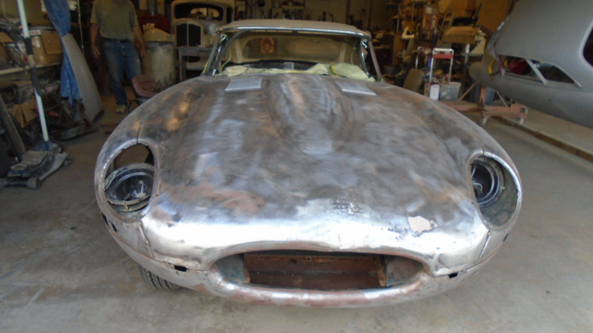 Front view of a silver Jaguar E-Type car body in a workshop, undergoing restoration.