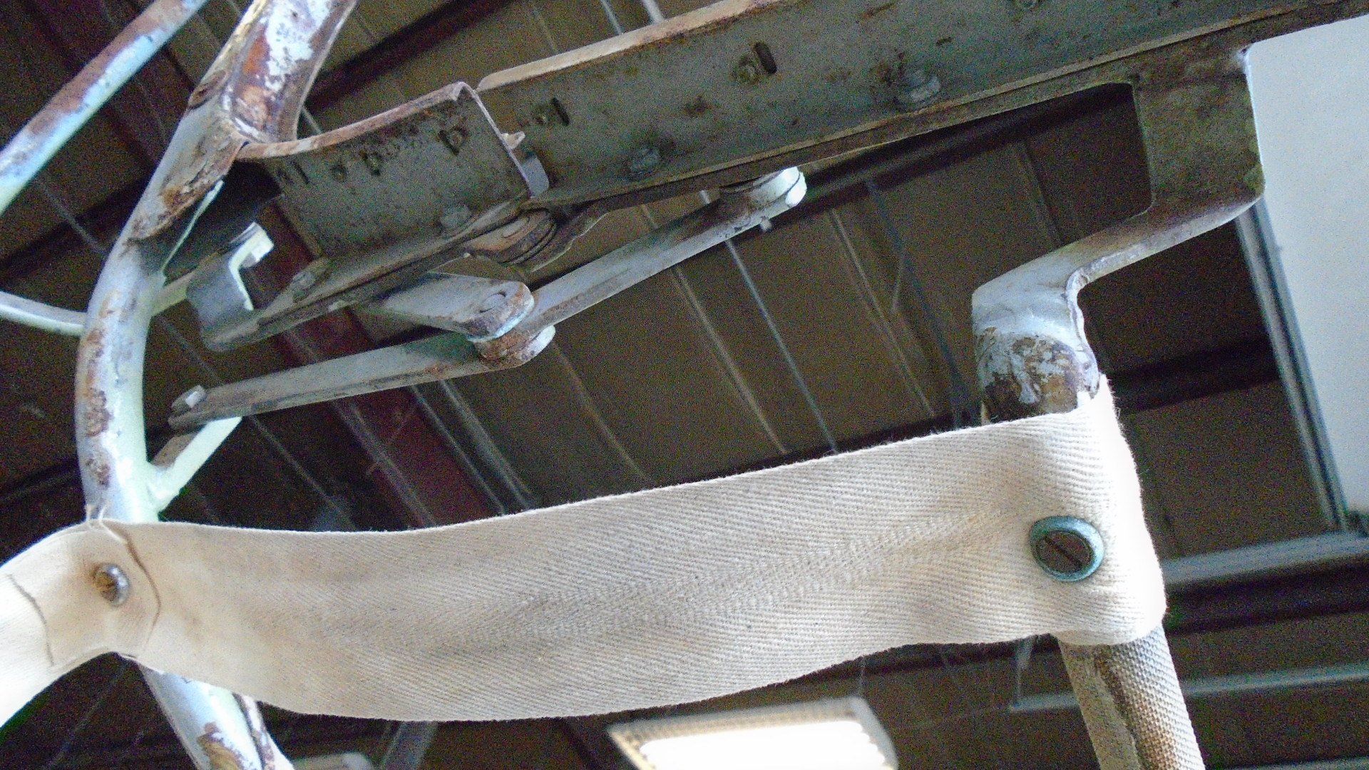 Close-up of a rusted metal frame with beige fabric attached by rivets.