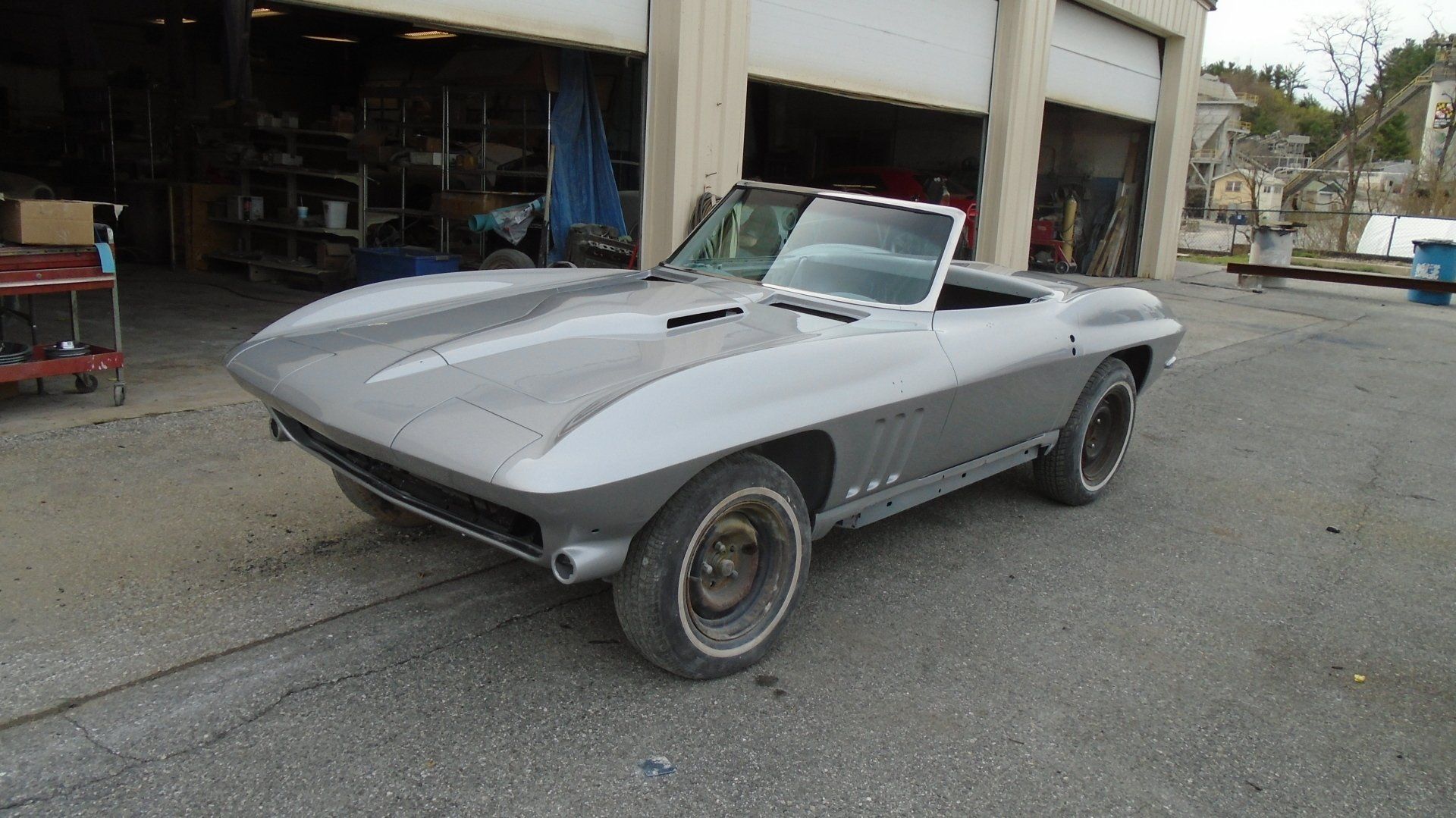 Gray classic Corvette convertible parked in front of a garage.