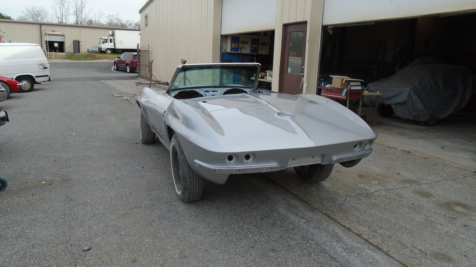 Silver classic convertible car outside a garage with open door.
