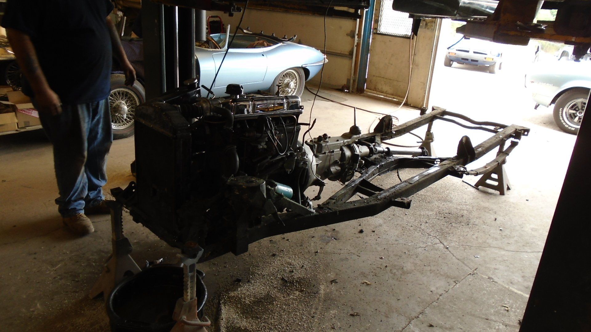 Engine and chassis of a vehicle being worked on in a garage. A person stands nearby.