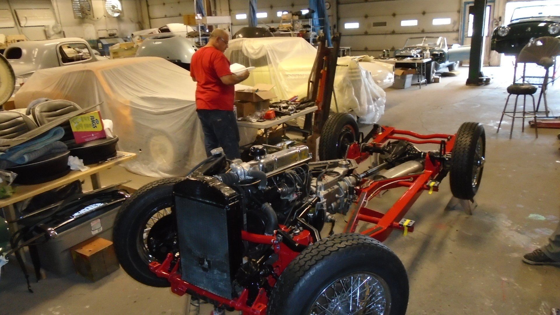 Man working on a red car chassis with engine in a garage. Car is partially assembled.