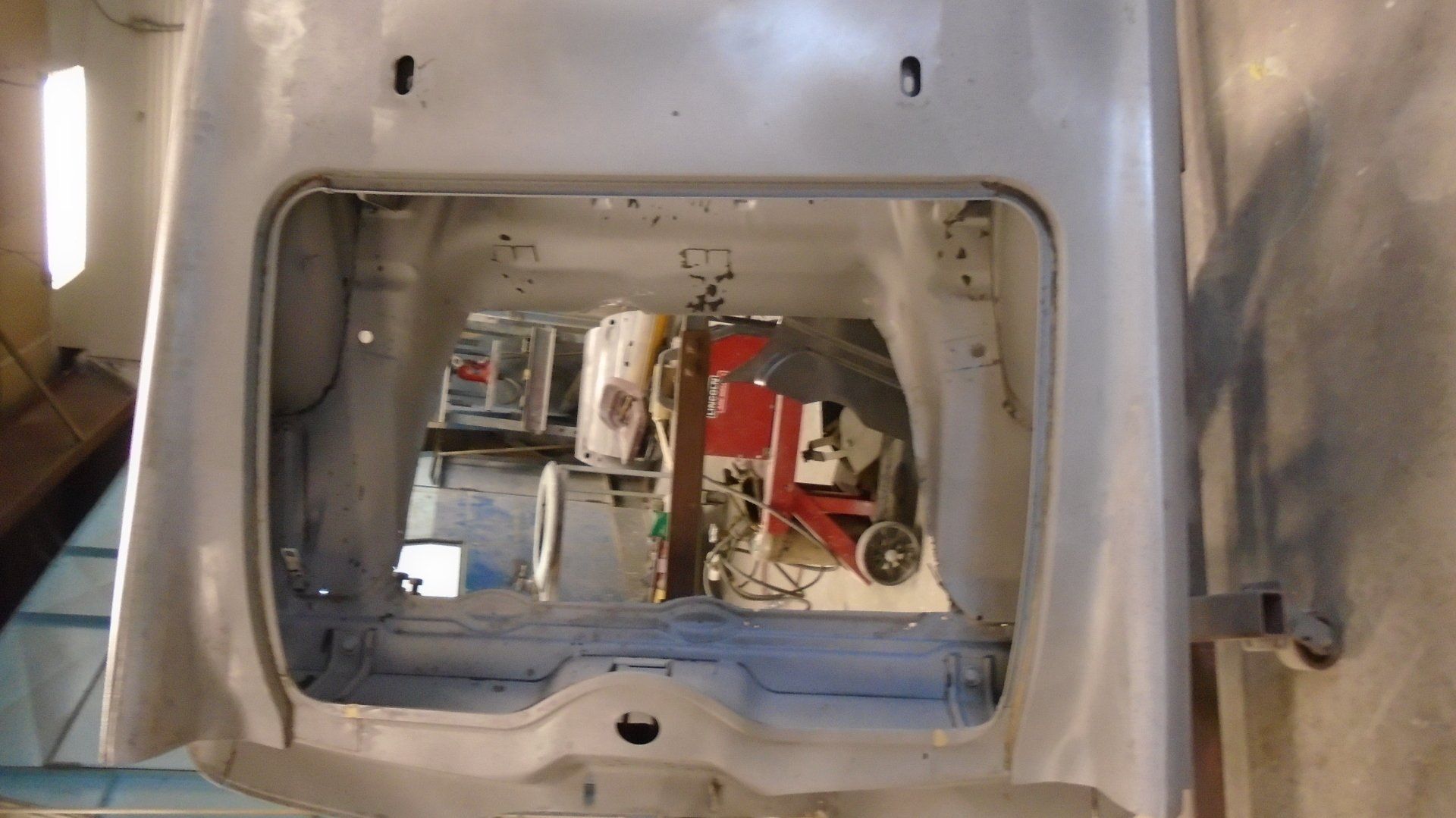 Empty car interior, light gray, with rectangular opening toward rear, showing tools and shop equipment inside.