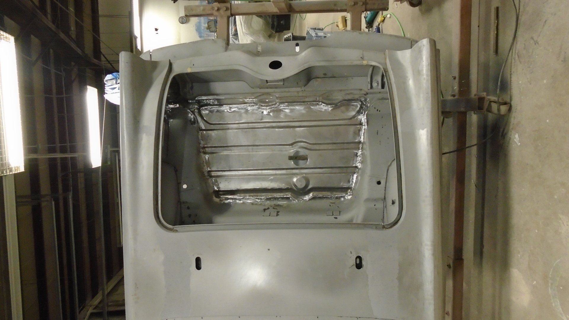 Bare metal car body, possibly a trunk area, viewed from the rear, prepared for restoration.