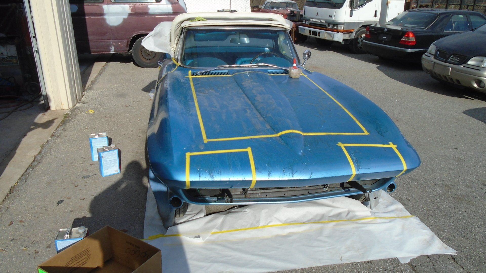 Blue convertible Corvette taped for paintwork in an outdoor setting.