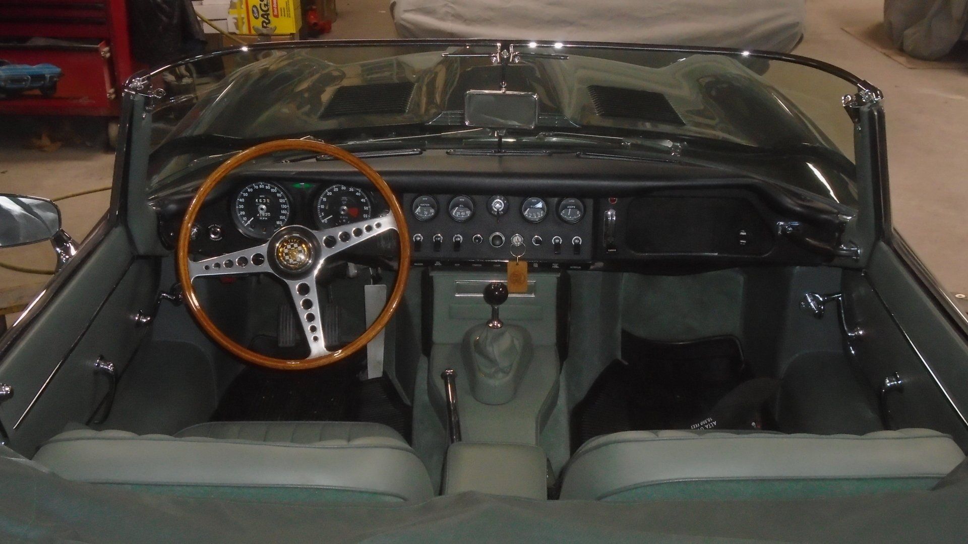 Interior of a classic green Jaguar E-Type convertible, showcasing a wood steering wheel, dashboard, and seats.
