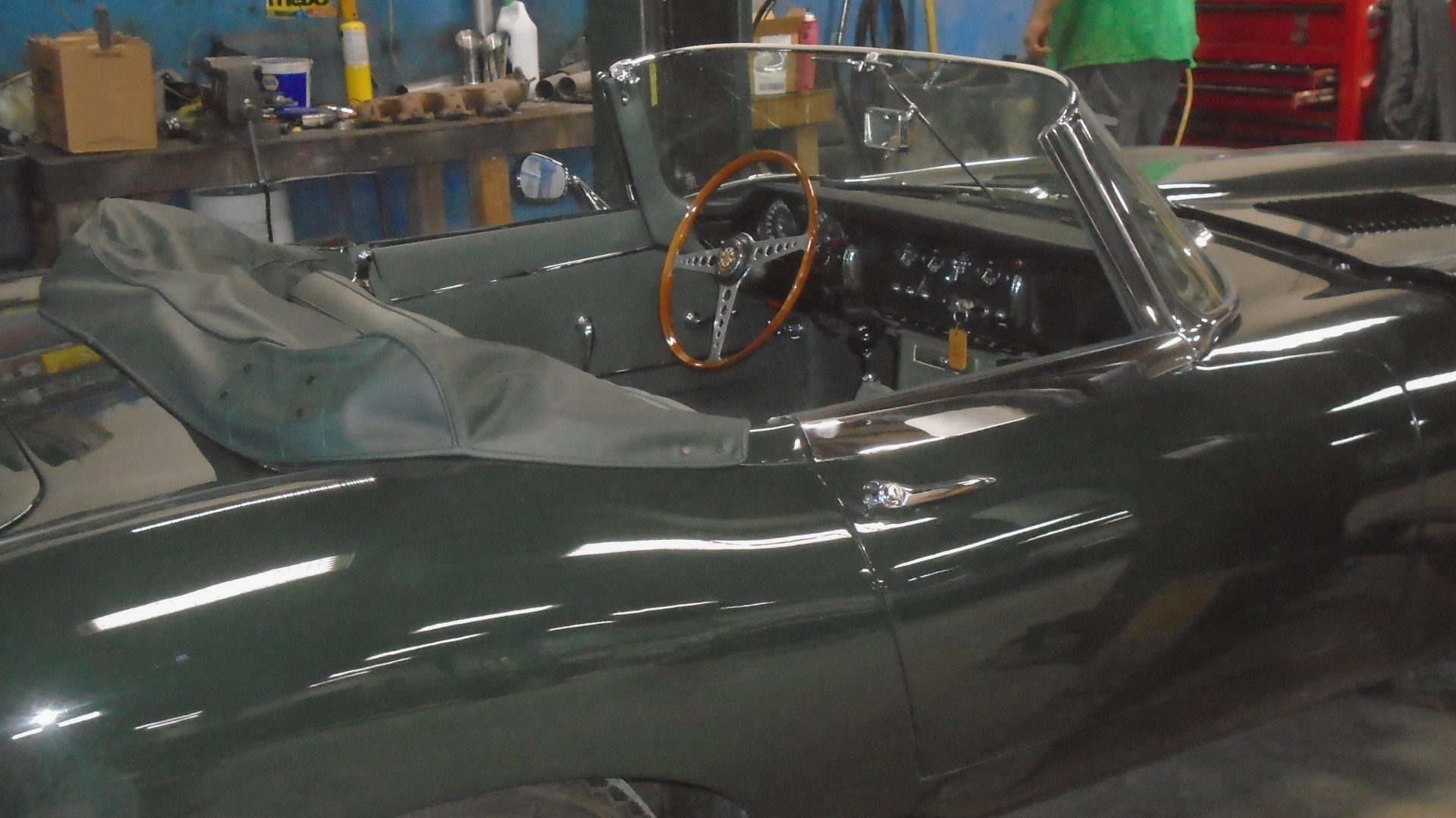 Dark green vintage convertible car interior, wooden steering wheel, soft top cover.