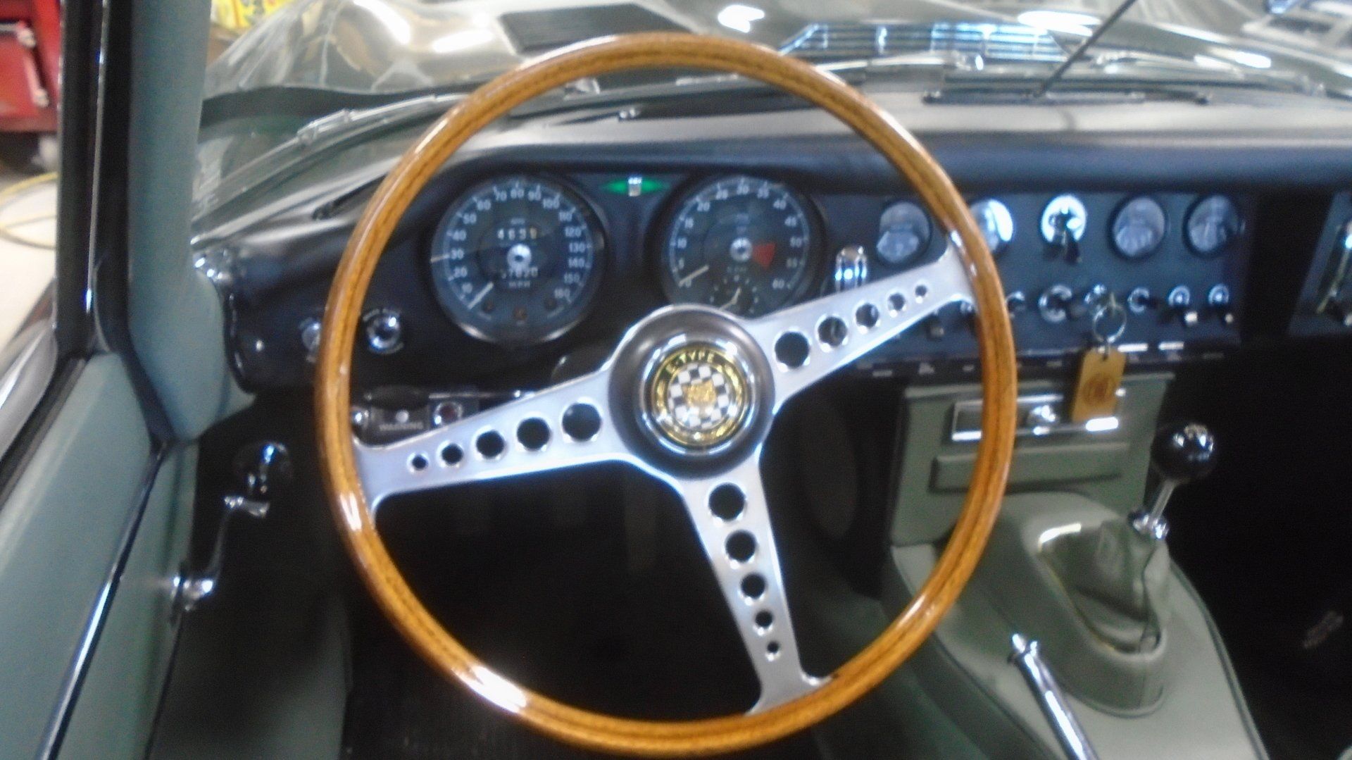 Classic car interior with wood-rimmed steering wheel, chrome spokes, and detailed dashboard gauges.