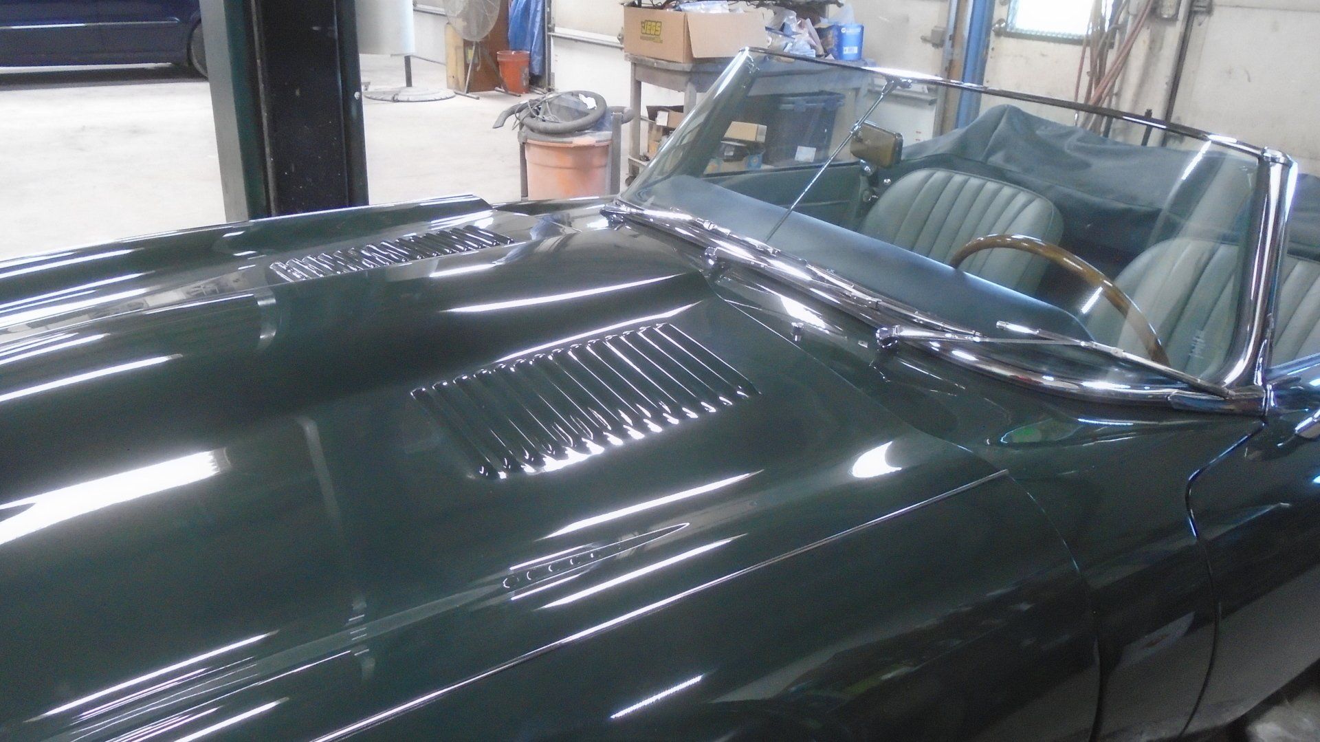 Green vintage convertible car in a garage, with visible hood vents and a windshield.