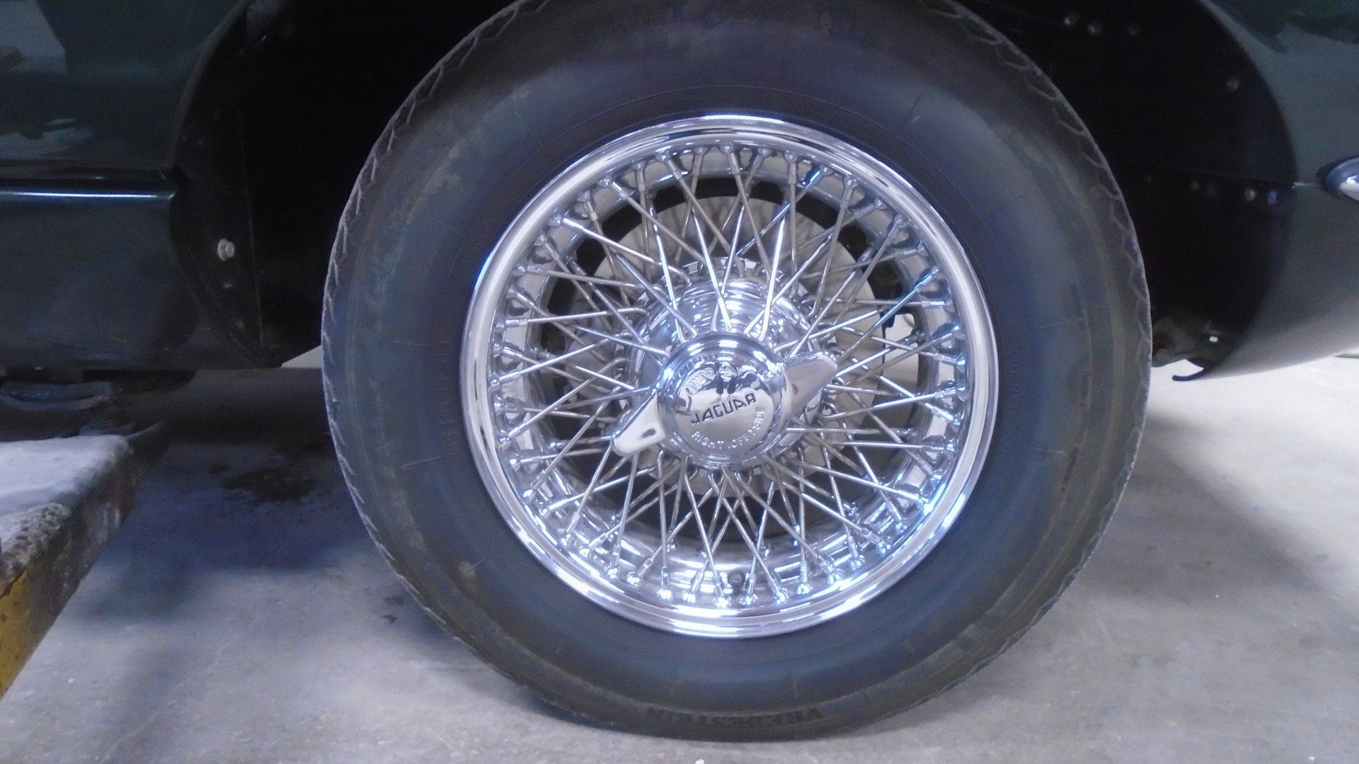 Shiny wire wheel on a dark green car, close-up view.