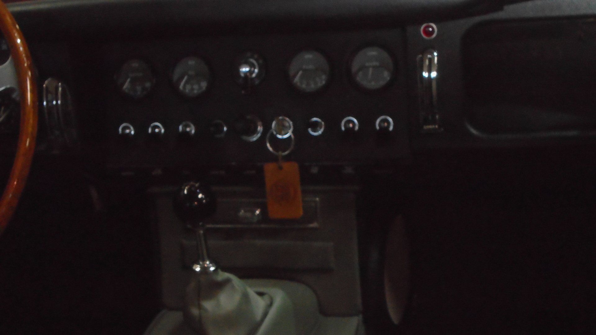 Interior dashboard of a classic car, black with several gauges, switches, and a key dangling.