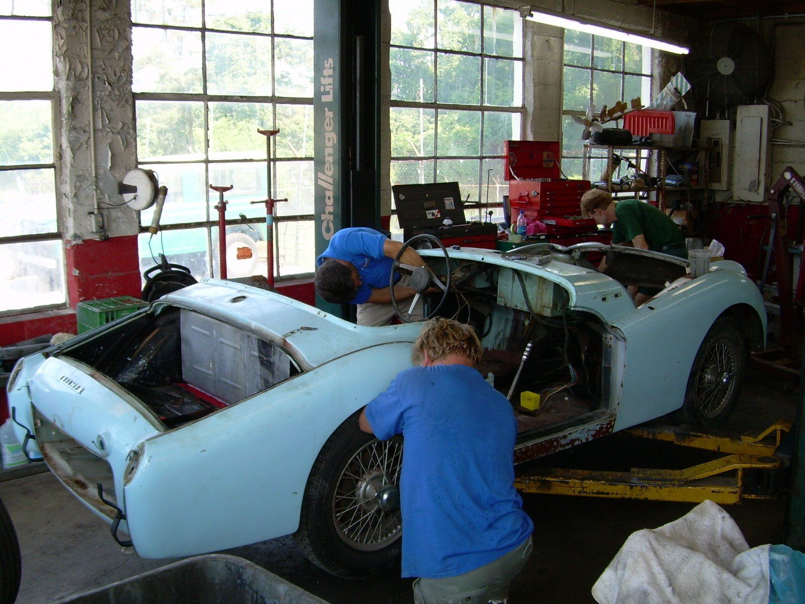 Mechanics working on a light blue vintage car inside a garage.