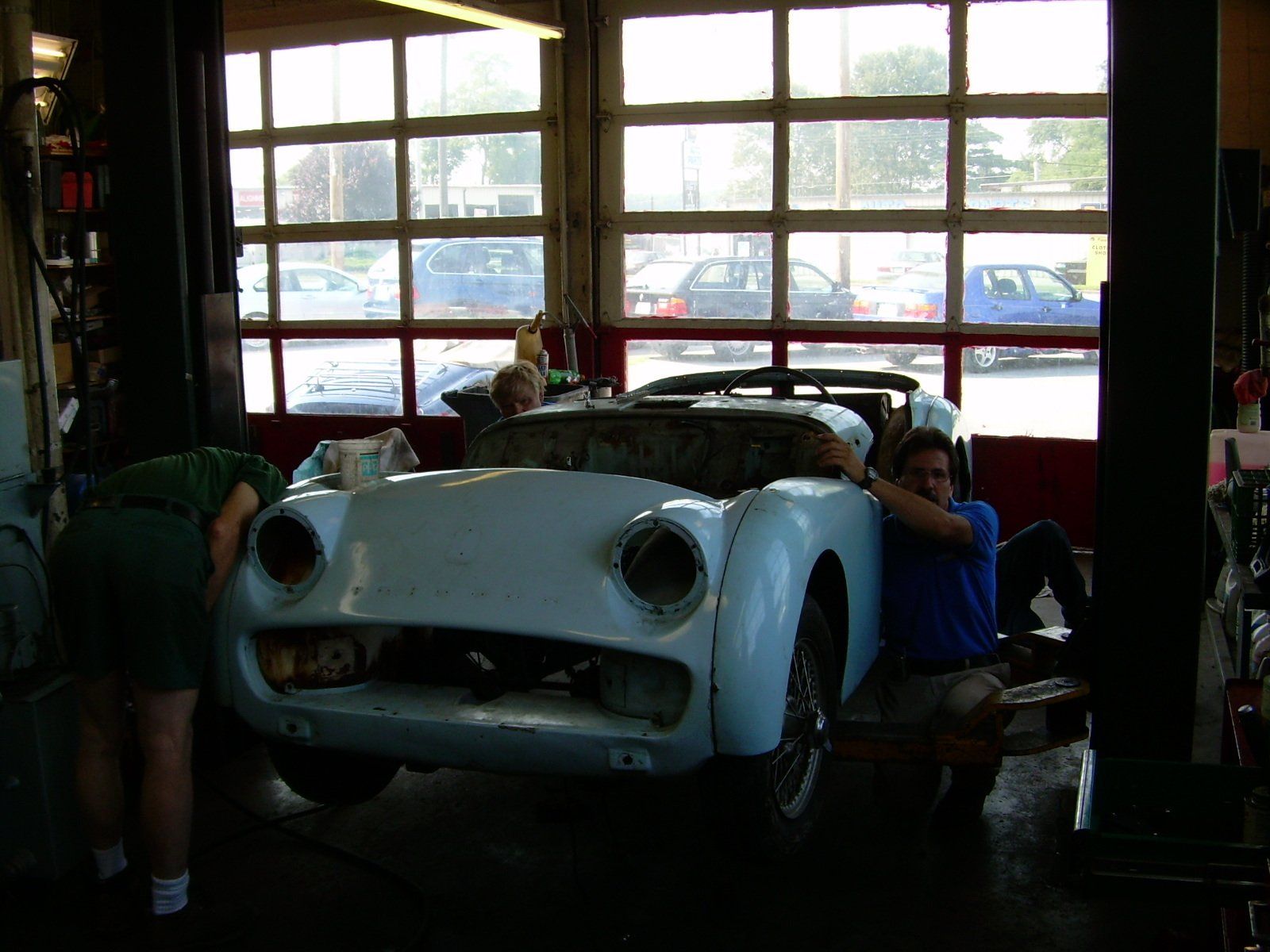 Two people working on a light blue vintage car in a garage.