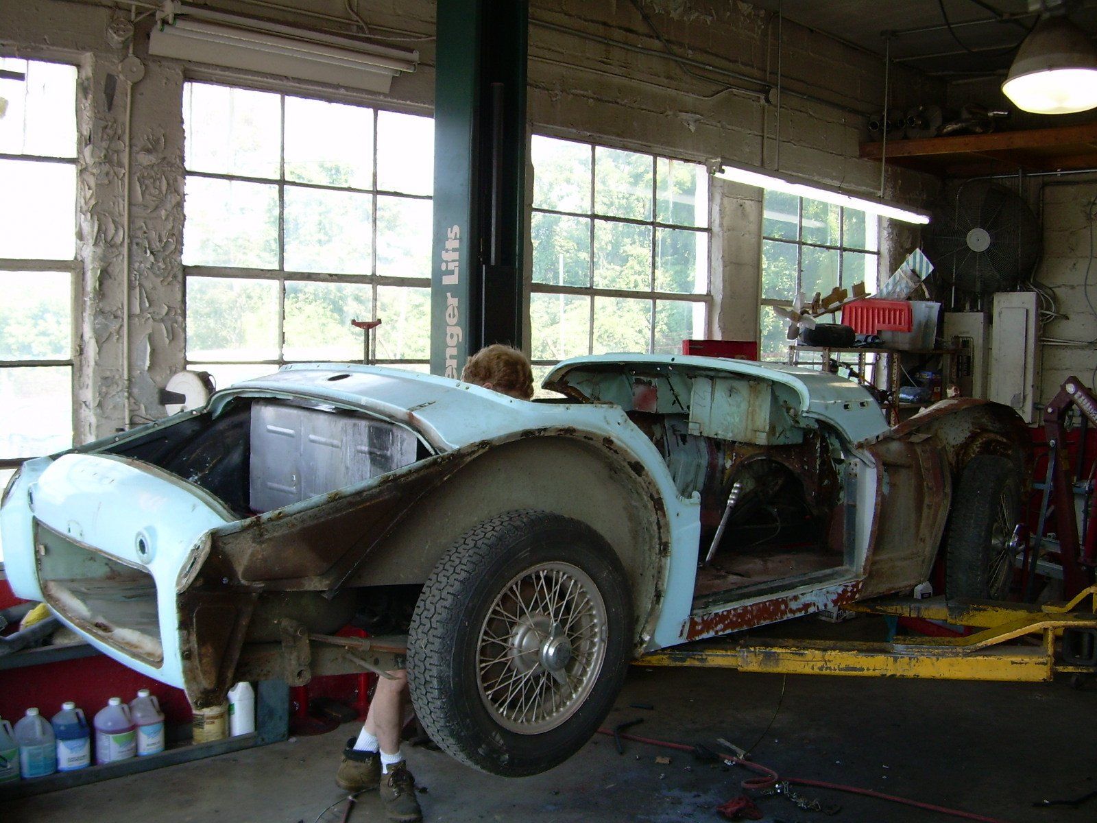 Classic light blue car body undergoing restoration in a garage, lifted on a hoist.