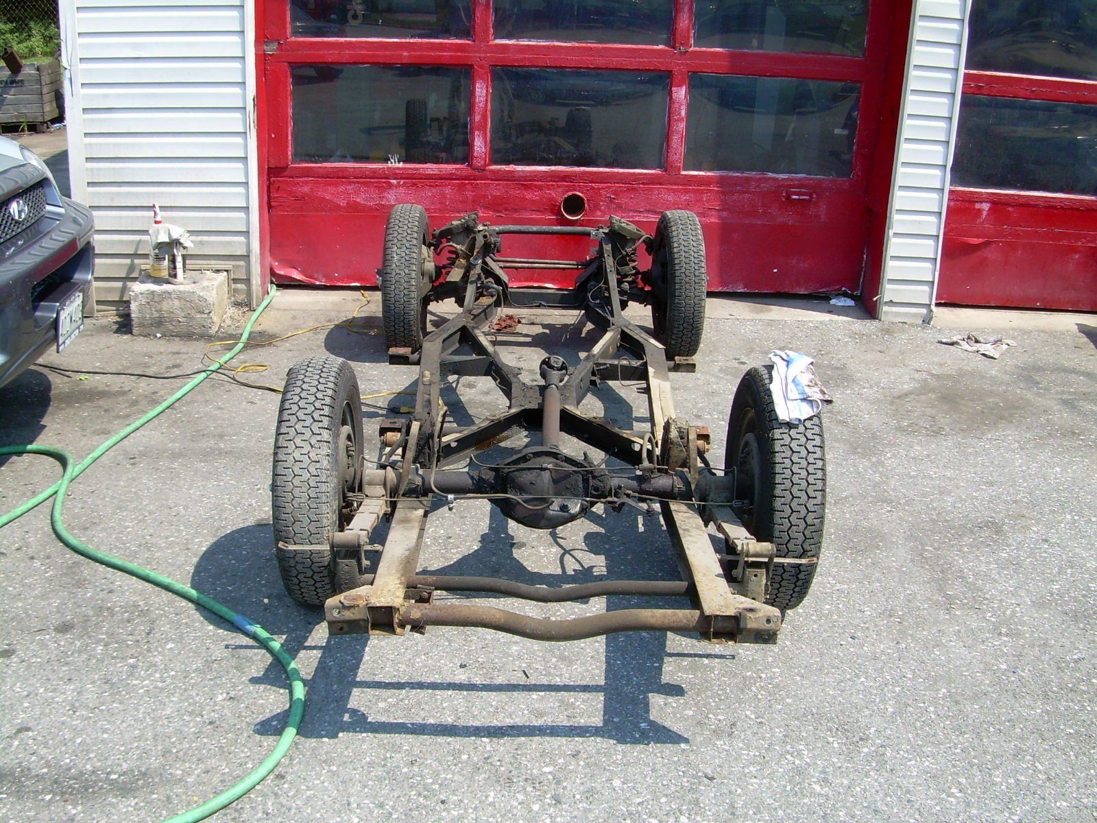 Car chassis with wheels, in front of a red garage door.