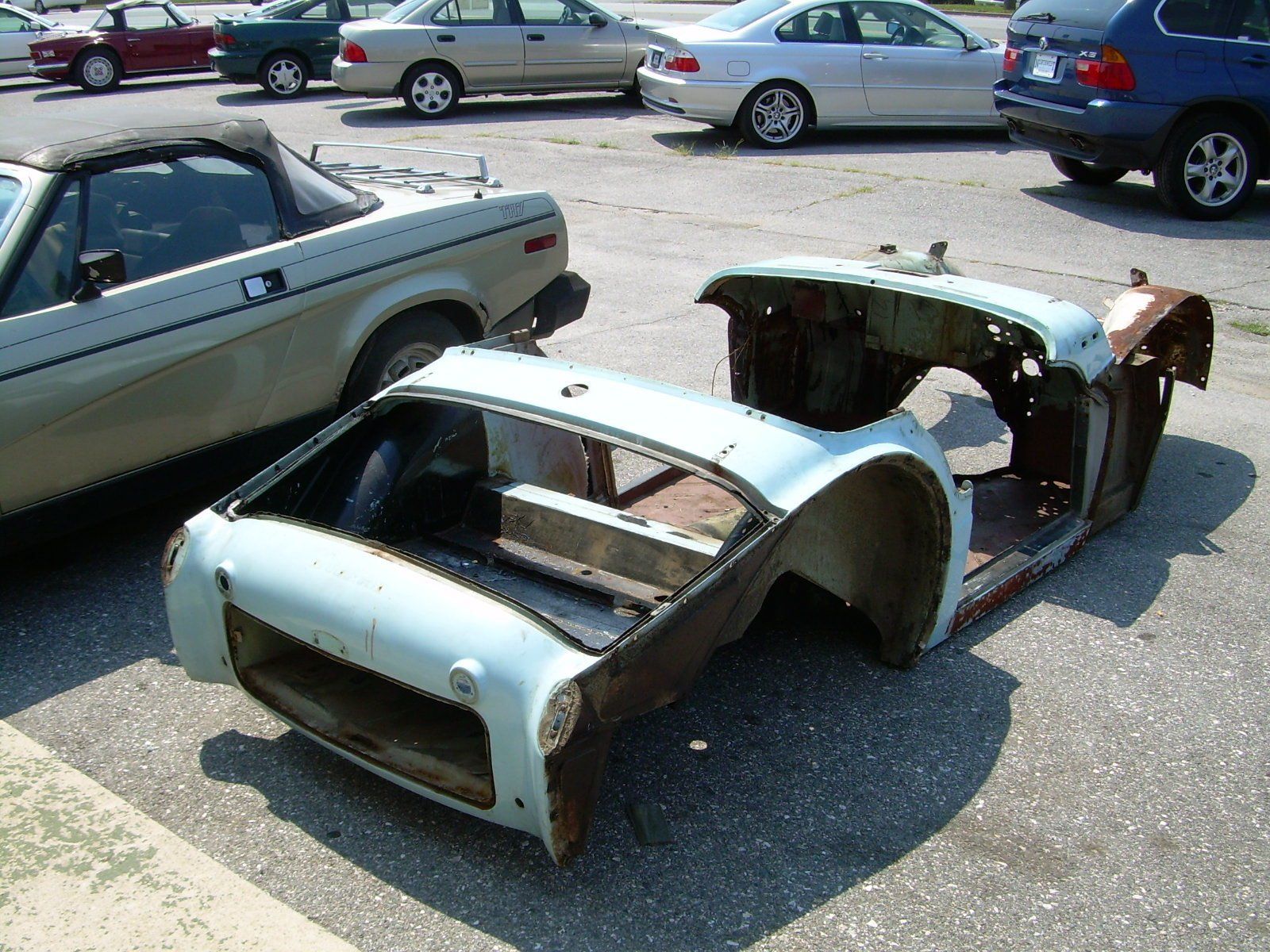Light blue car body shell with significant rust, parked outdoors.