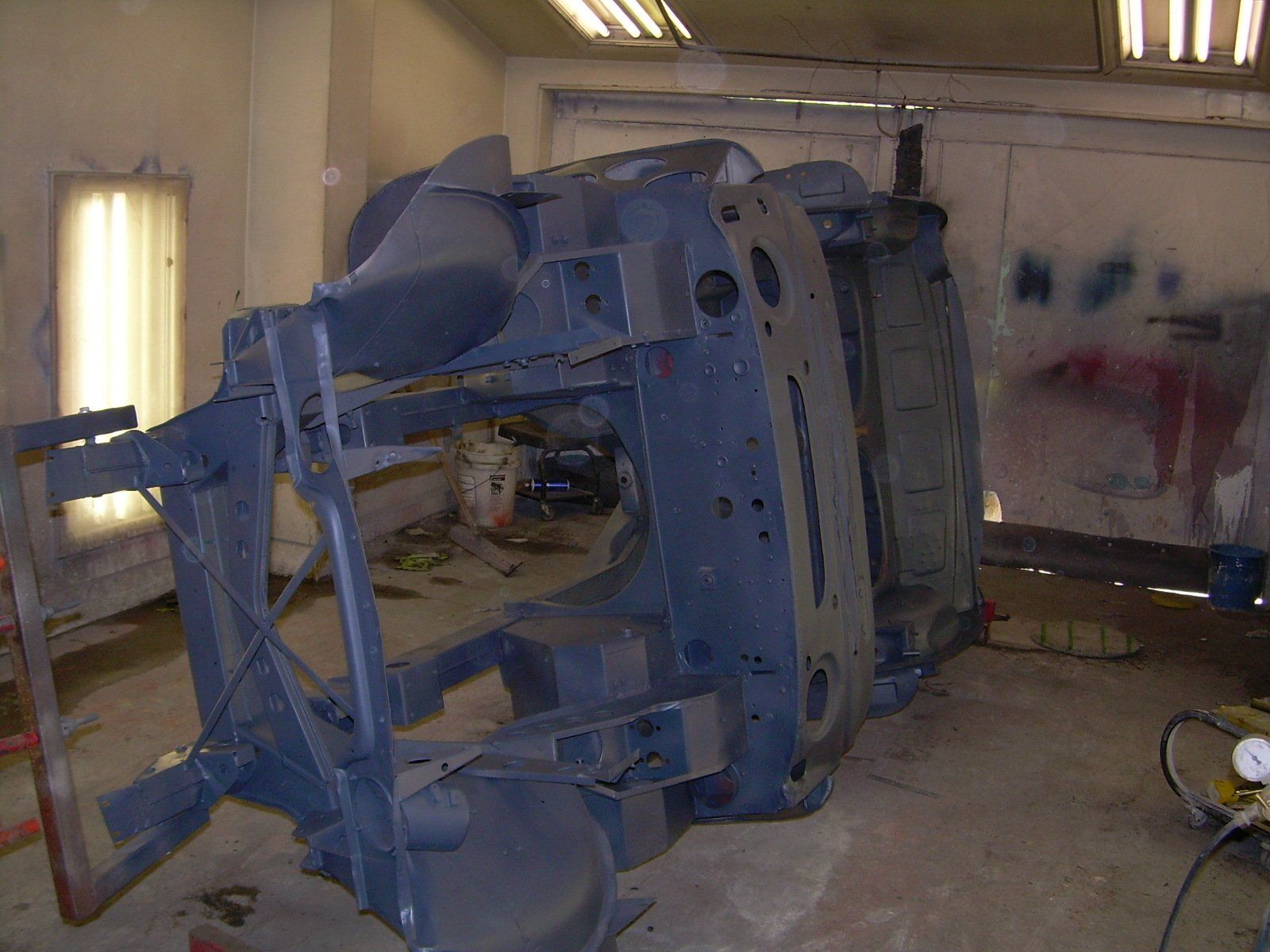 Car chassis upside down in a spray booth, painted dark blue.