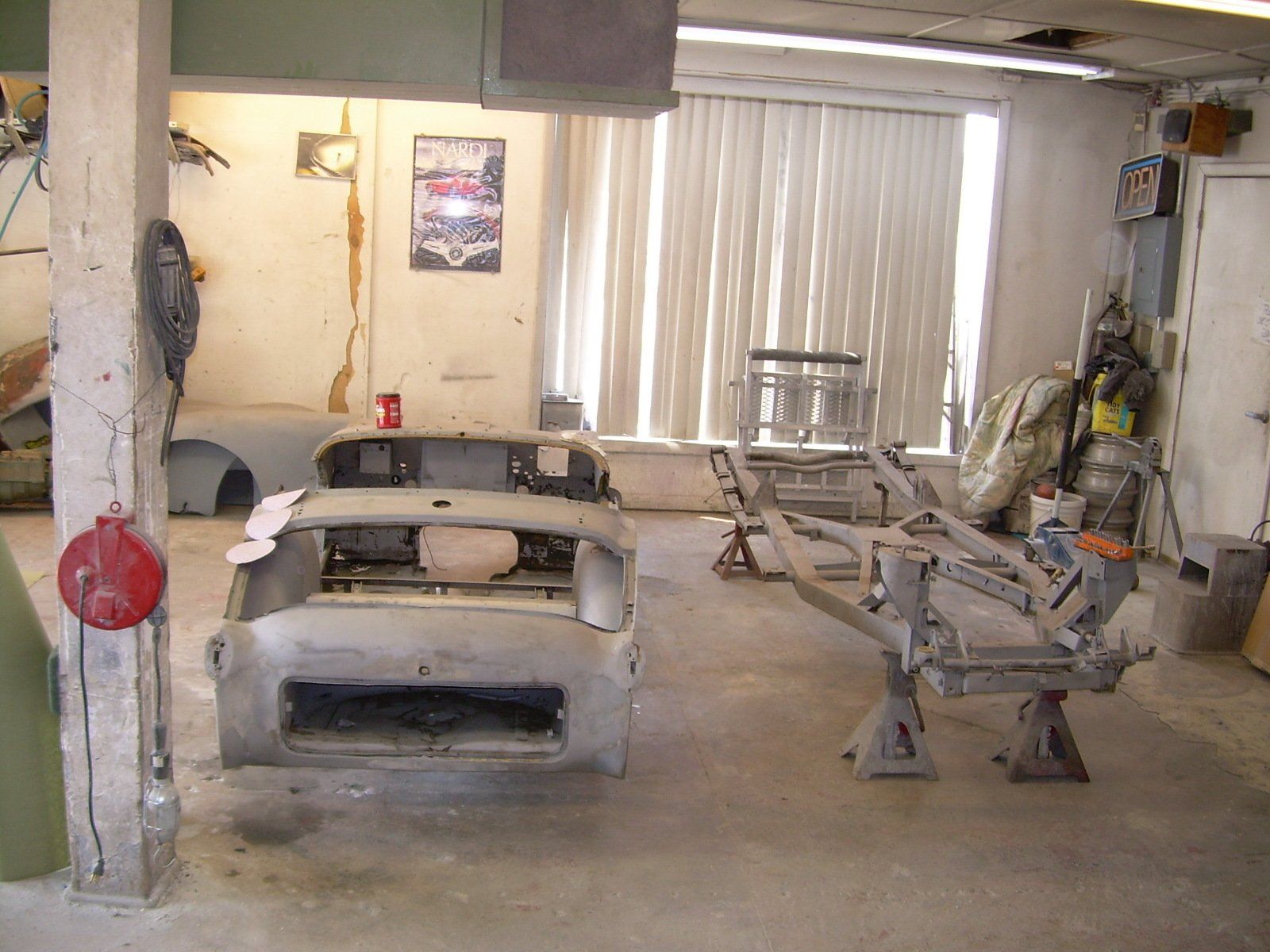 Car parts inside a workshop, including a chassis on stands and a disassembled body.